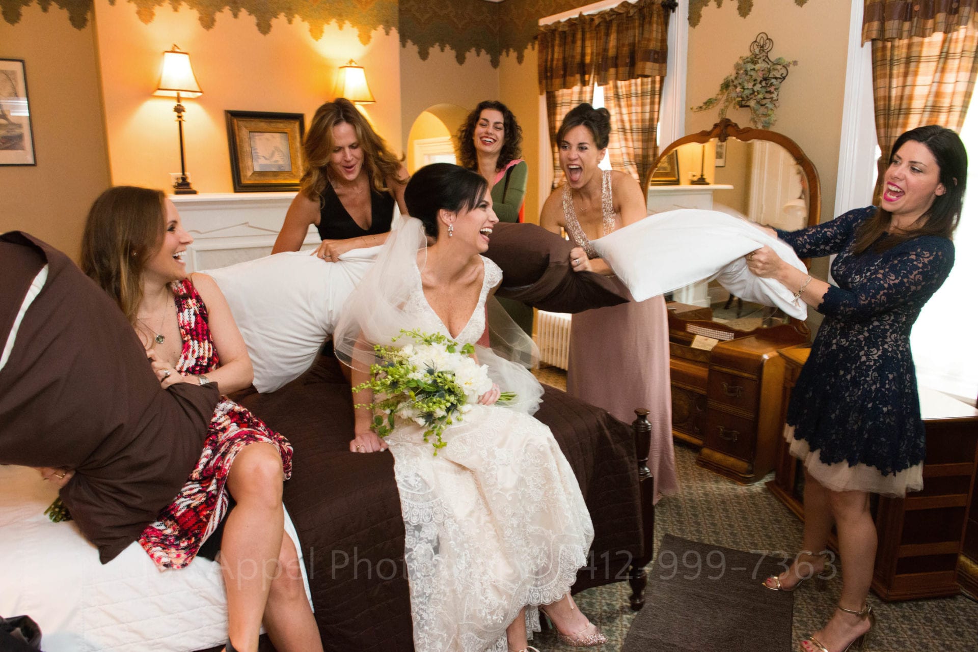 a group of laughing women surround a bride while having a pillow fight in a bedroom. Wedding Photography In West Virginia.