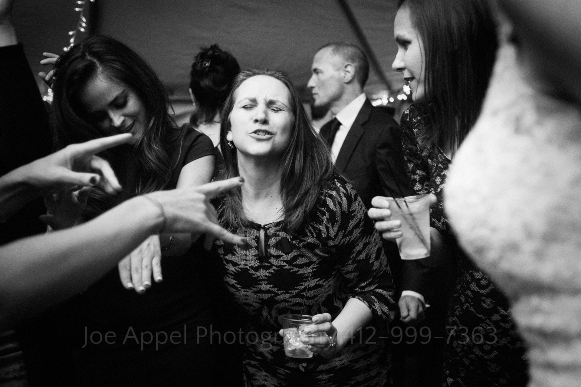 A woman closes her eyes and sings while dancing. Two hands come in from the left side of the frame and point at her. Wedding Photography In West Virginia.