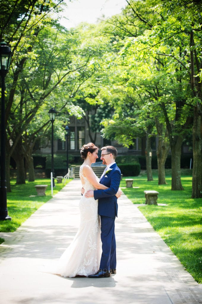 A bride and groom stand close facing each other on a stone pathway covered by trees.