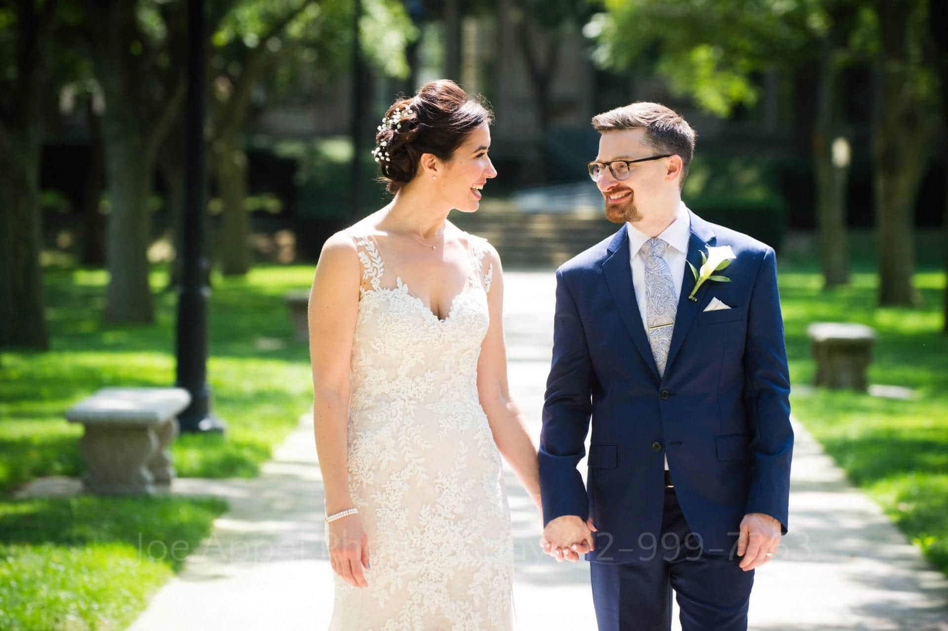 A bride and groom walk and hold hands on a flagstone pathway.