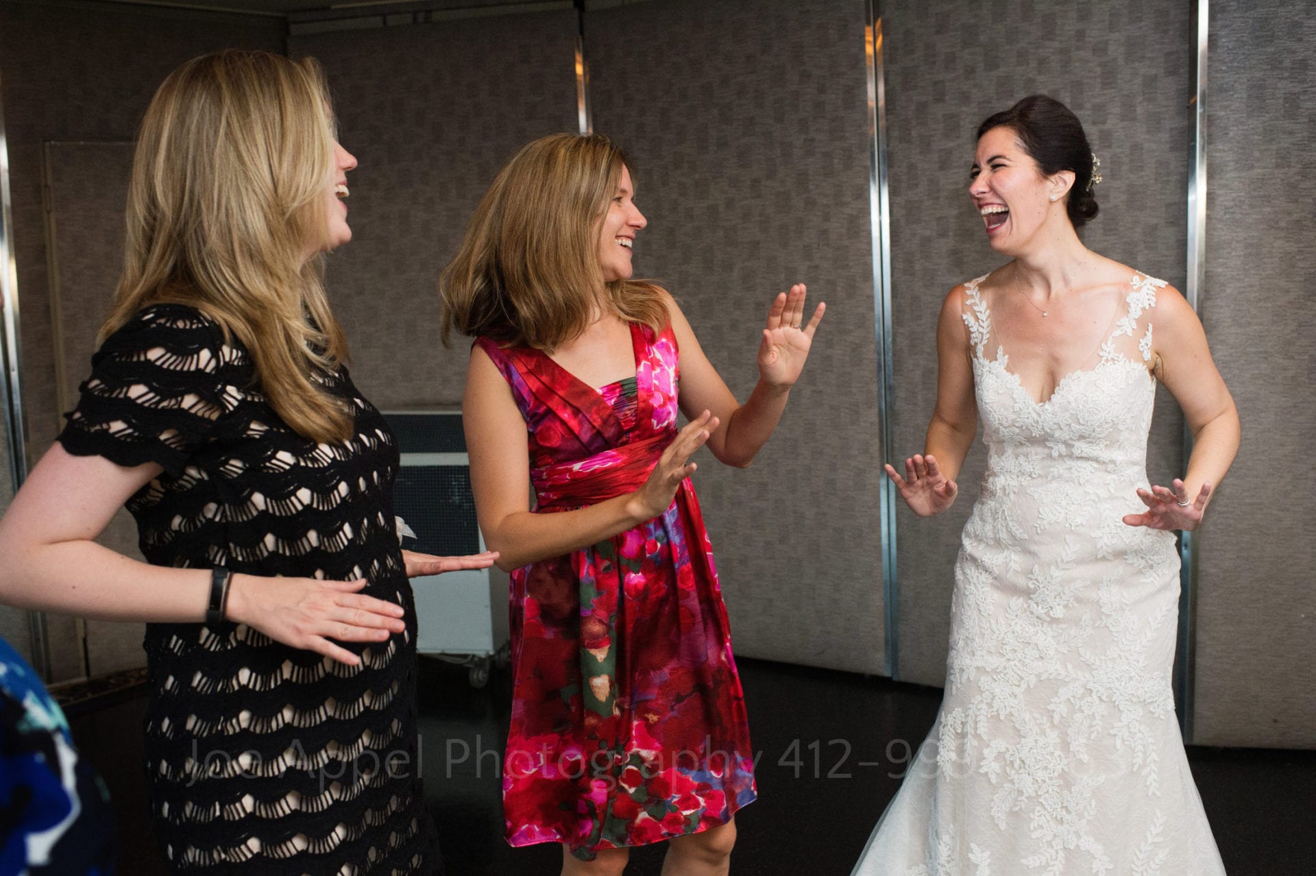 A bride in a white dress laughs as she dances with two other women
