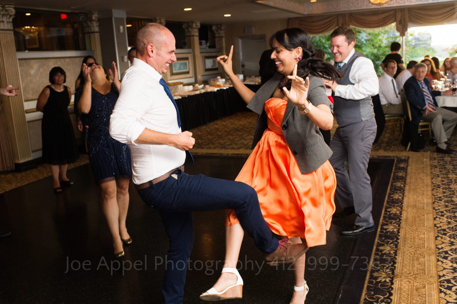 A woman in an orange dress and a man in a white shirt hook their legs together as they dance.