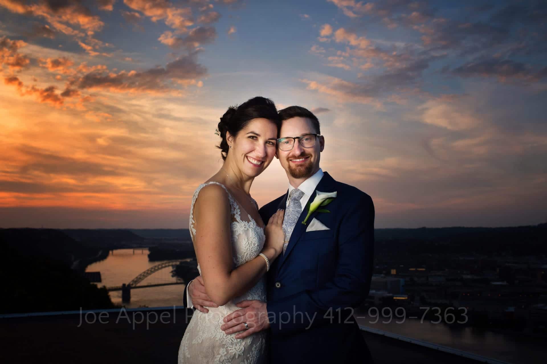 With a dramatic sunset behind them, a couple stands with their heads touching.