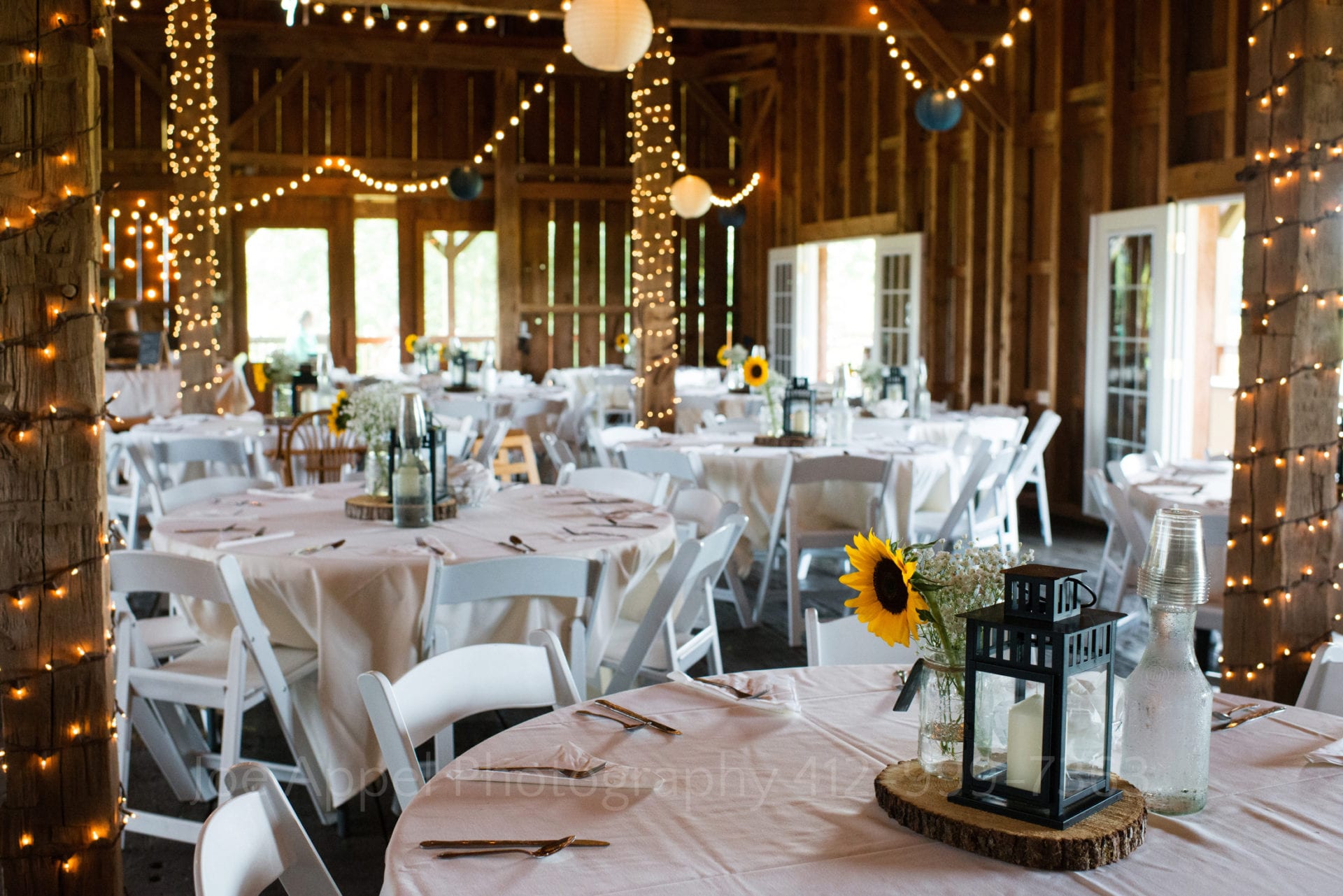 sunflowers and twinkle lights accent the white tablecloth covered interior of a barn set up for an Armstrong Farms Weddings