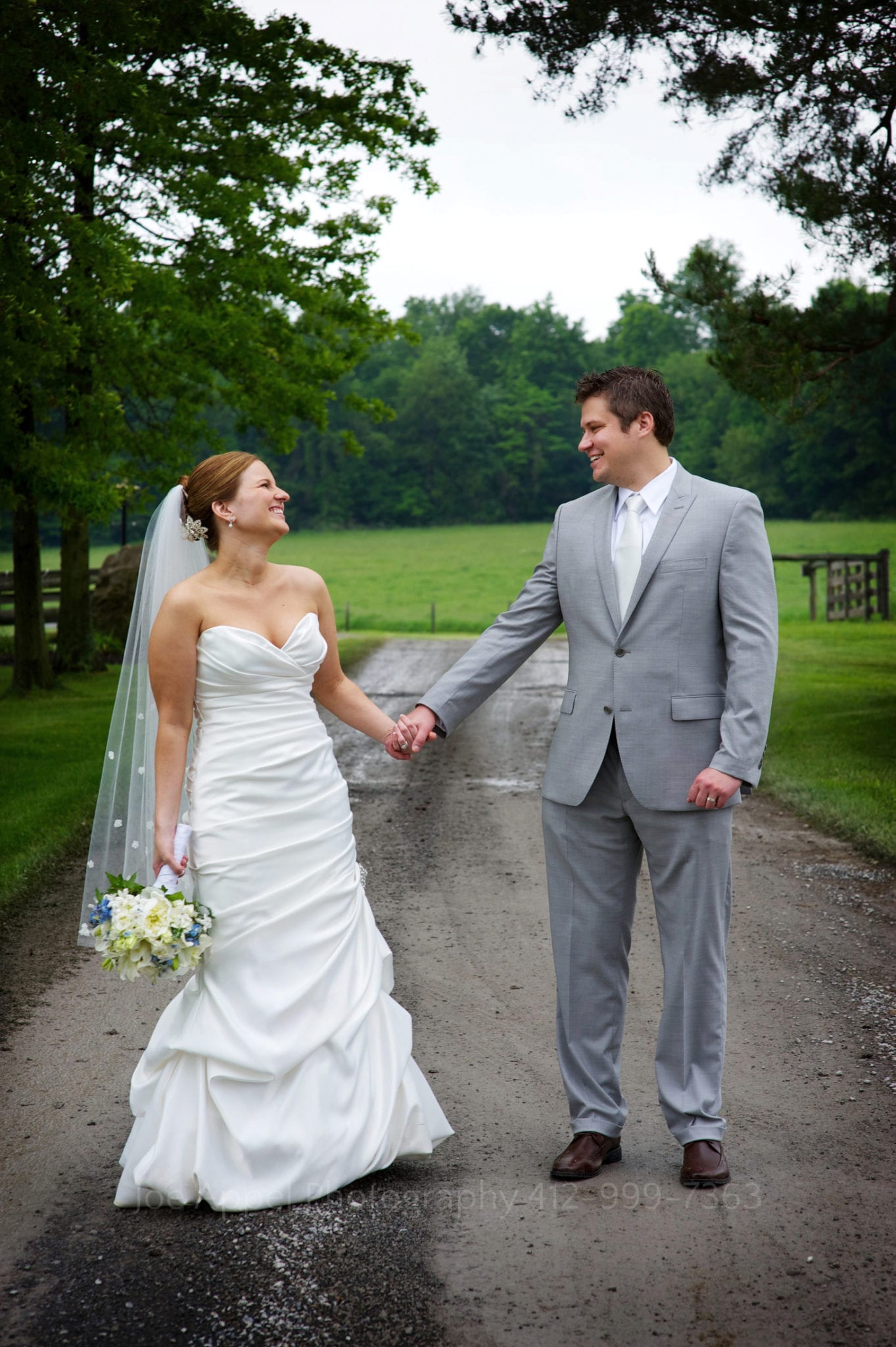 A bride and groom hold hands on a rain-soaked gravel road. Armstrong Farms Weddings
