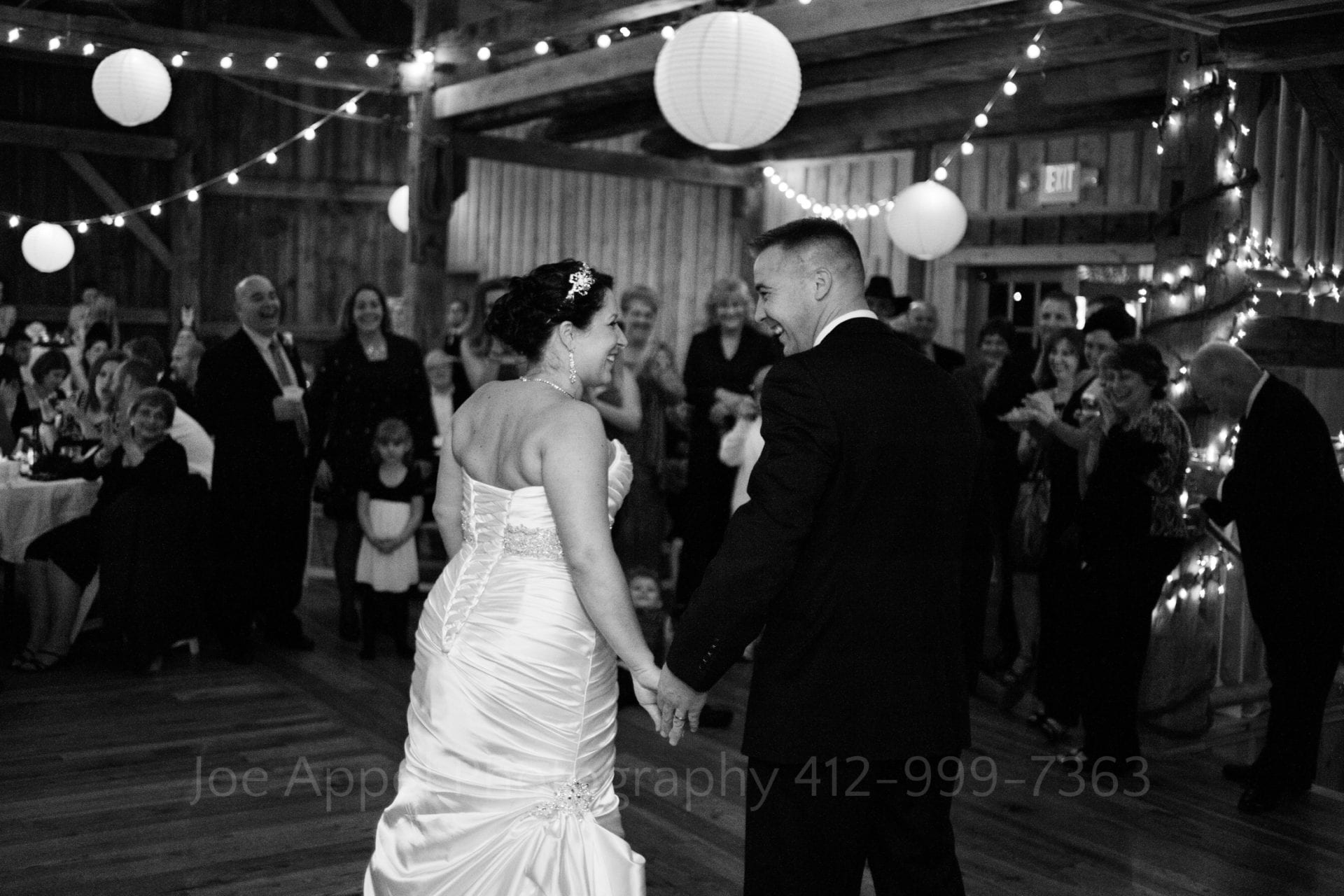 A bride and groom hold hands as they walk to the dance floor surrounded by applauding guests. Armstrong Farms Weddings