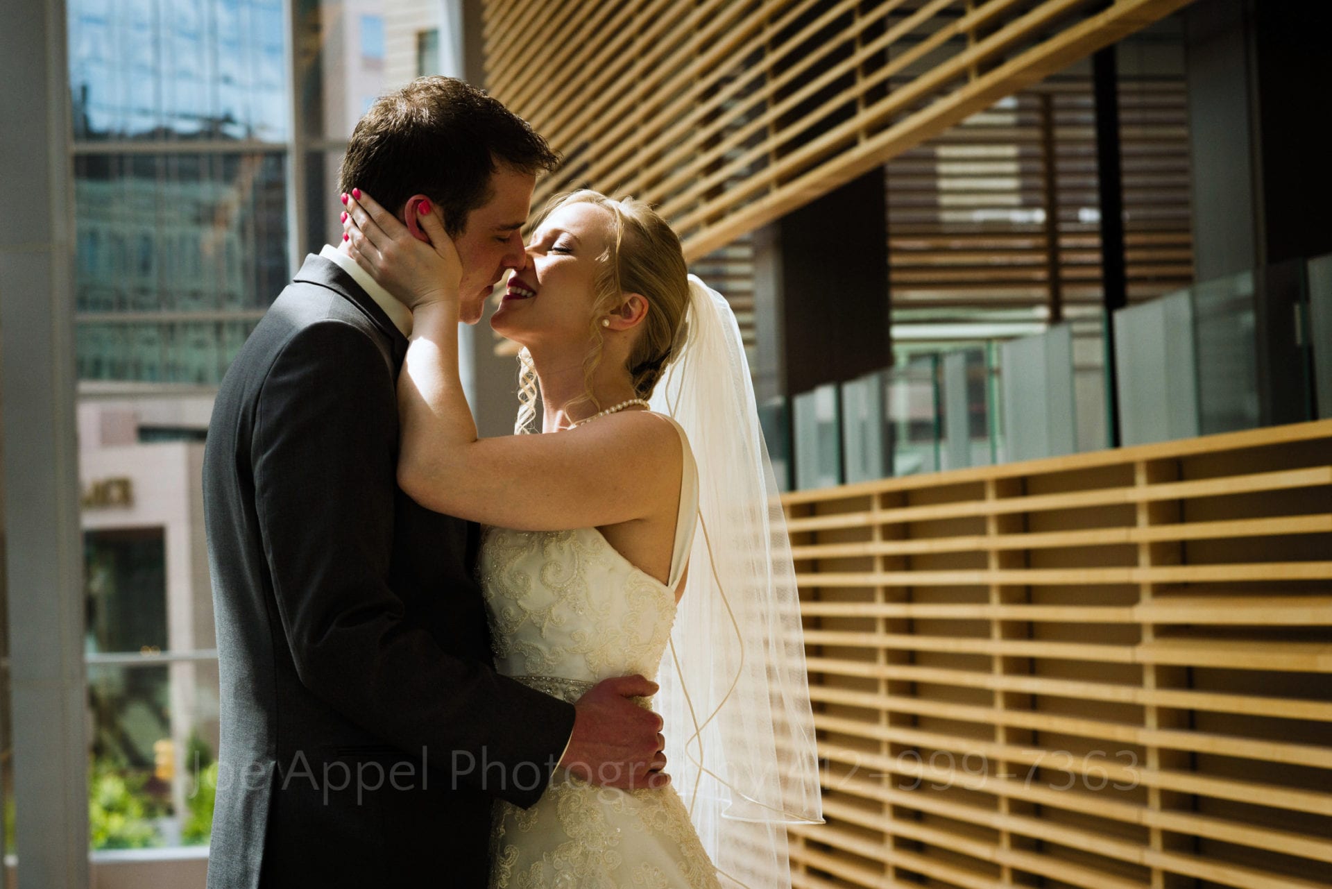 bride and groom embrace for a kiss on a stairway with decorative wooden slats in the background Fairmont Hotel Pittsburgh Weddings