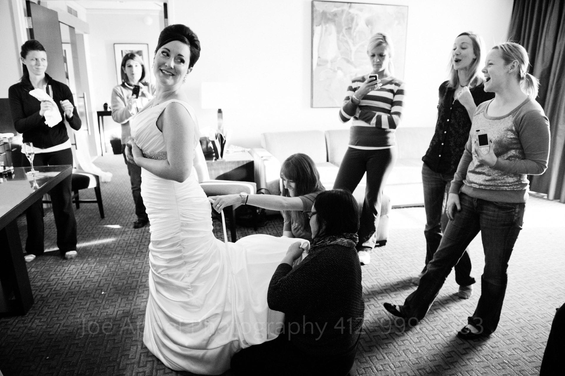 A bride looks over her shoulder as her friends work on the train of her dress and other friends stand watching Fairmont Hotel Pittsburgh Weddings.