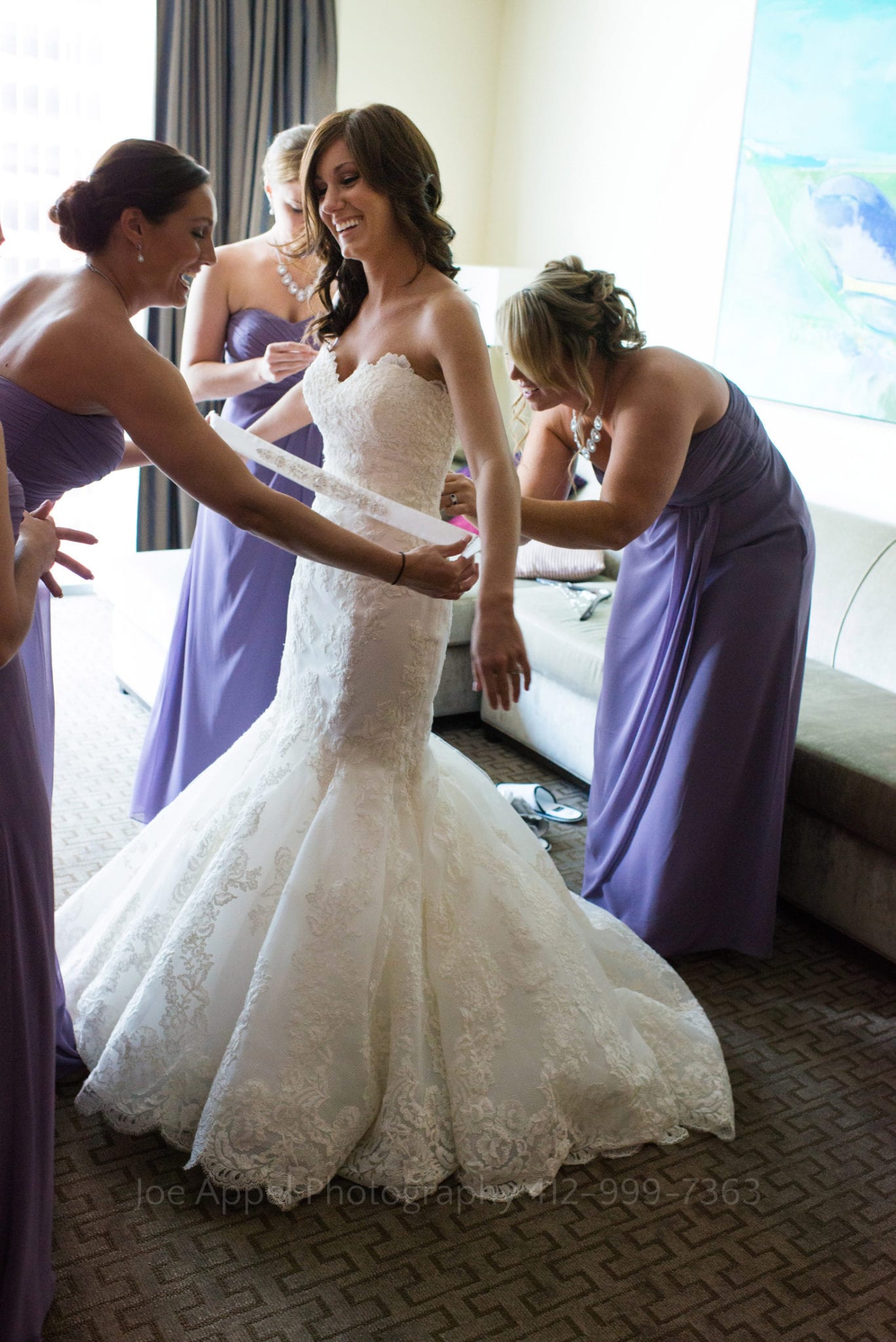 a bride is helped into her dress by her bridesmaids dressed in purple Fairmont Hotel Pittsburgh Weddings