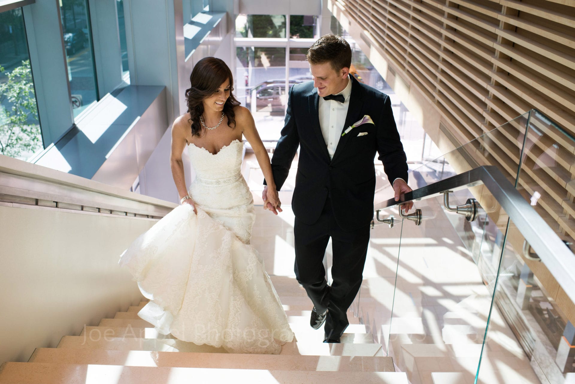 A bride and groom hold hands as they walk up a white staircase Fairmont Hotel Pittsburgh Weddings
