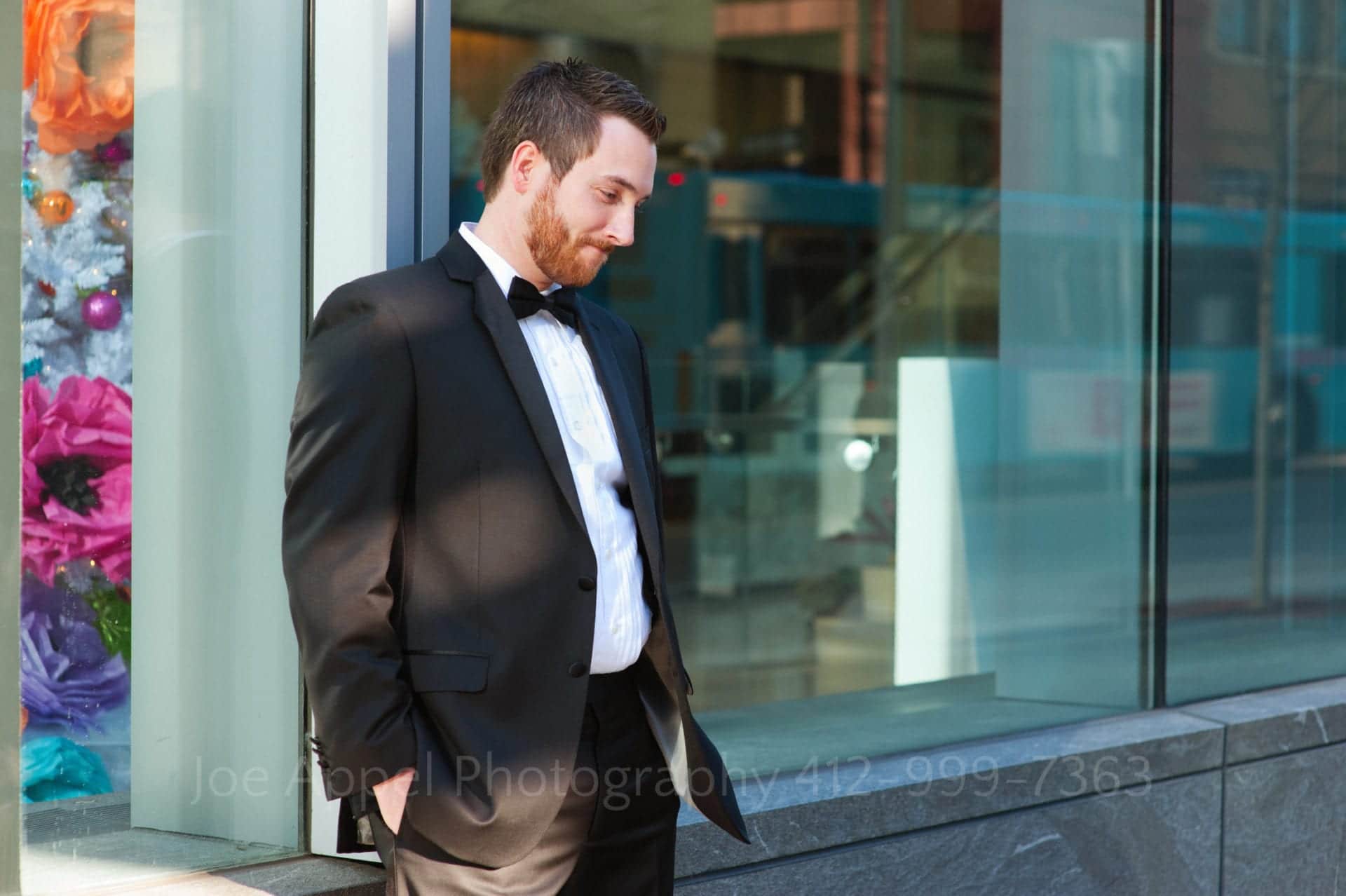 A tuxedoed man leans against a window as he stands with his hands in his pockets Fairmont Hotel Pittsburgh Weddings.