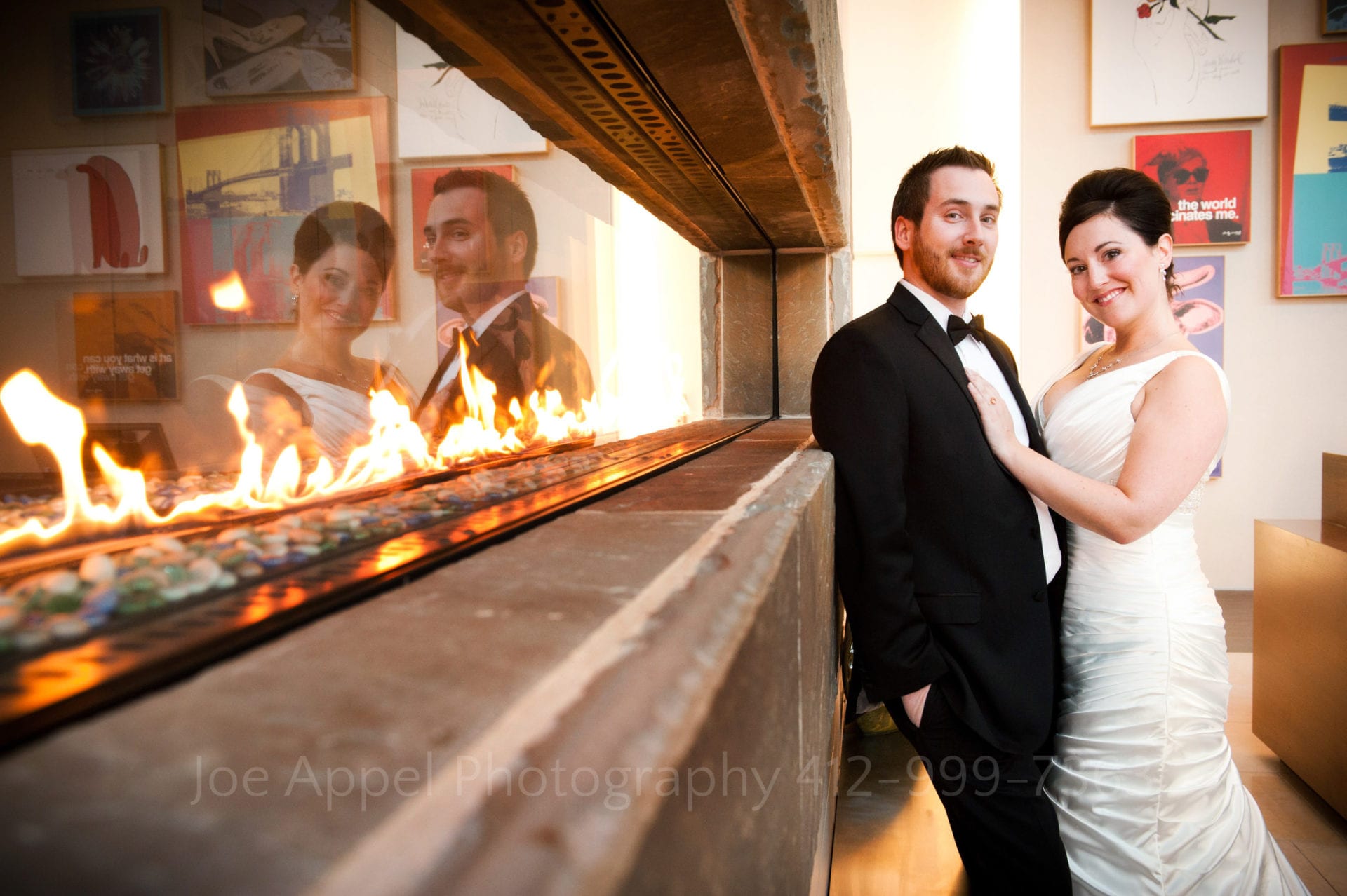 A bride and groom stand next to a long, glass fireplace which they are reflected in Fairmont Hotel Pittsburgh Weddings.