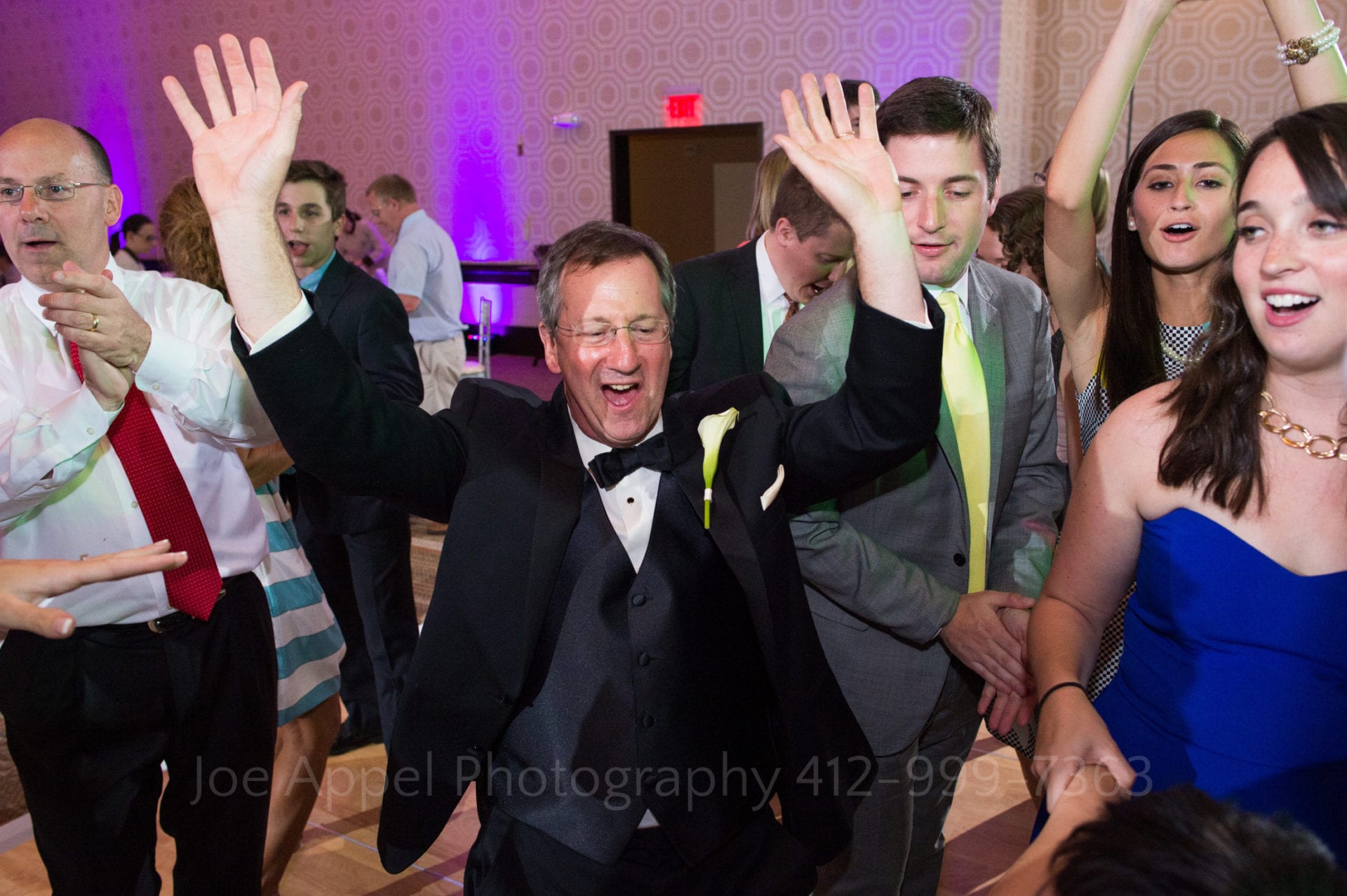 A man holds his hands in the air as he dances with a group of wedding guests Fairmont Hotel Pittsburgh Weddings