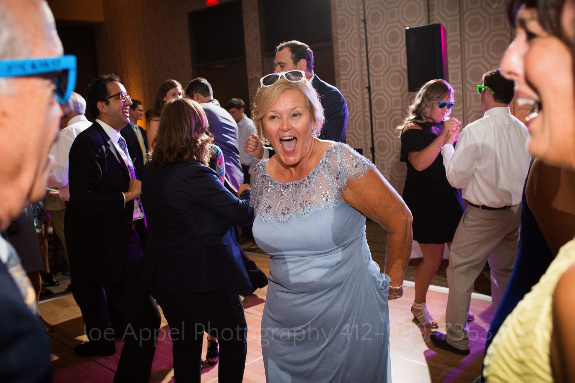 A woman wearing a light blue dress laughs as she dances with a man and a woman in a yellow dress Fairmont Hotel Pittsburgh Weddings.