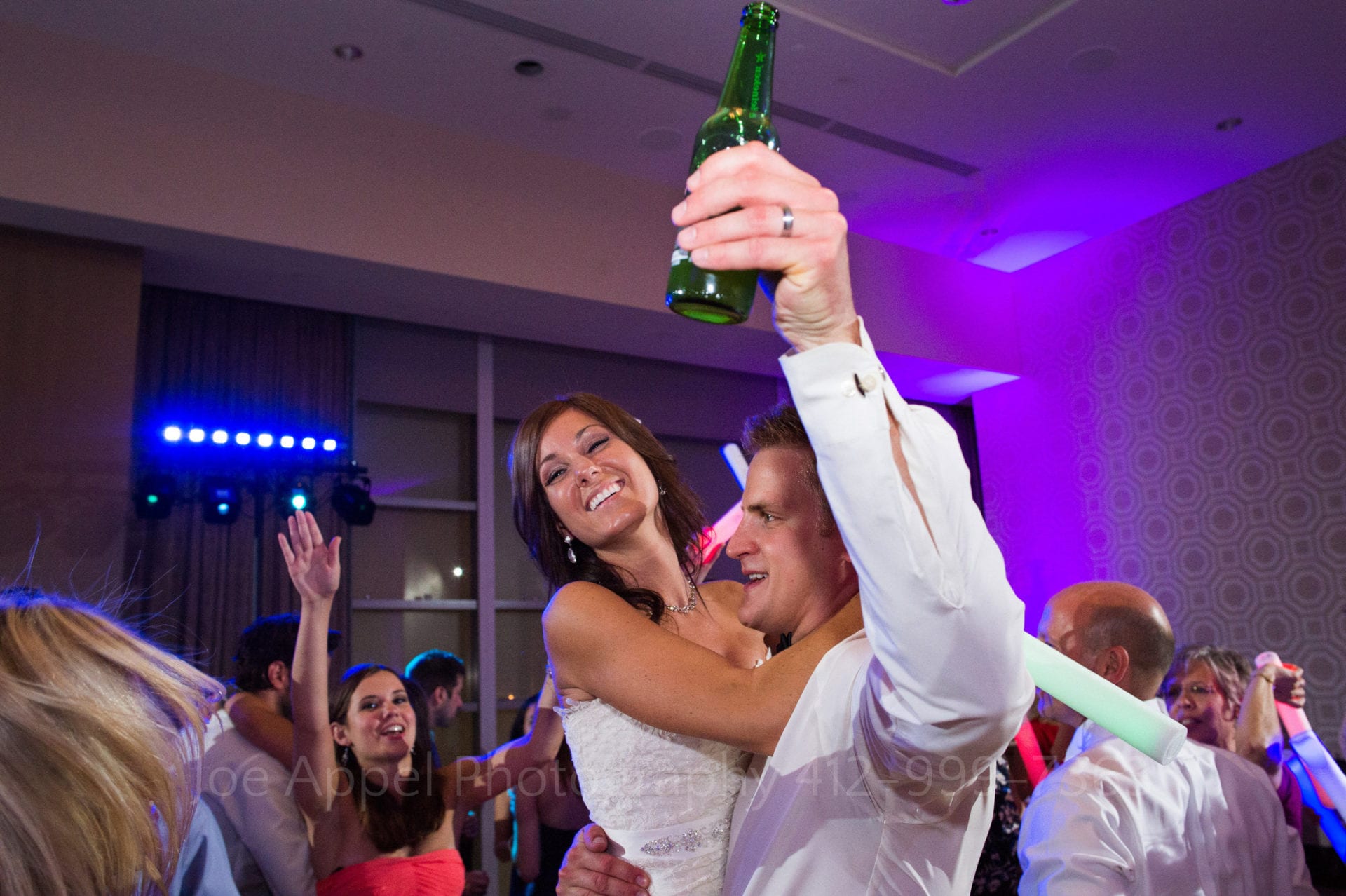 a groom holds his beer bottle in one hand and lifts his smiling bride in his other hand. Fairmont Hotel Pittsburgh Weddings