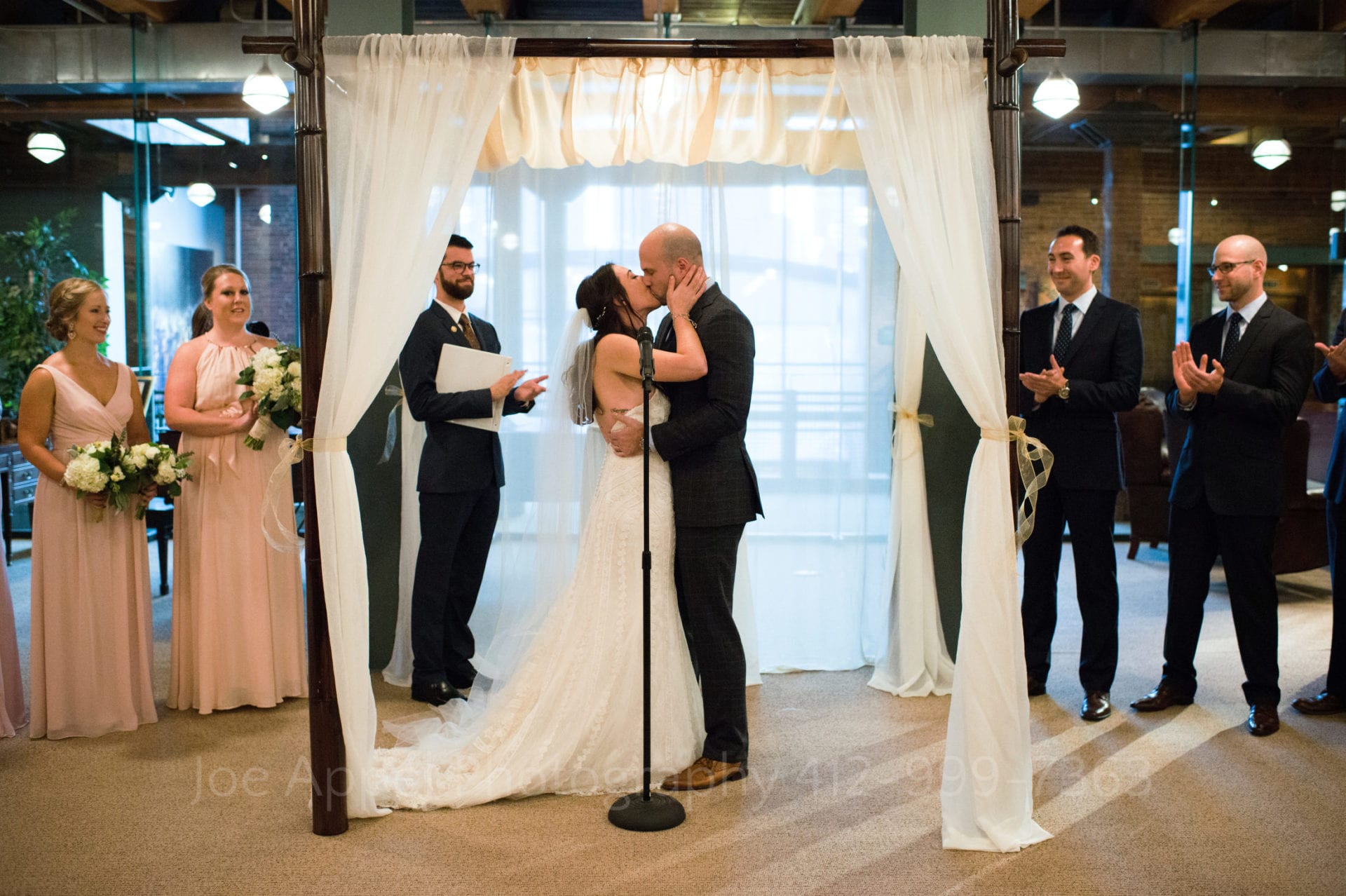 Bride and groom kiss beneath a chuppah in the Library & Archives Reading Room at the Heinz History Center