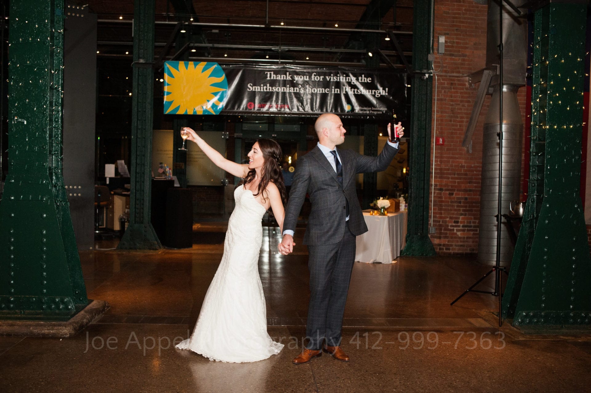 A couple enters the Great Hall at the Heinz History Center and turn away from each other while holding their glasses up to toast their guests.