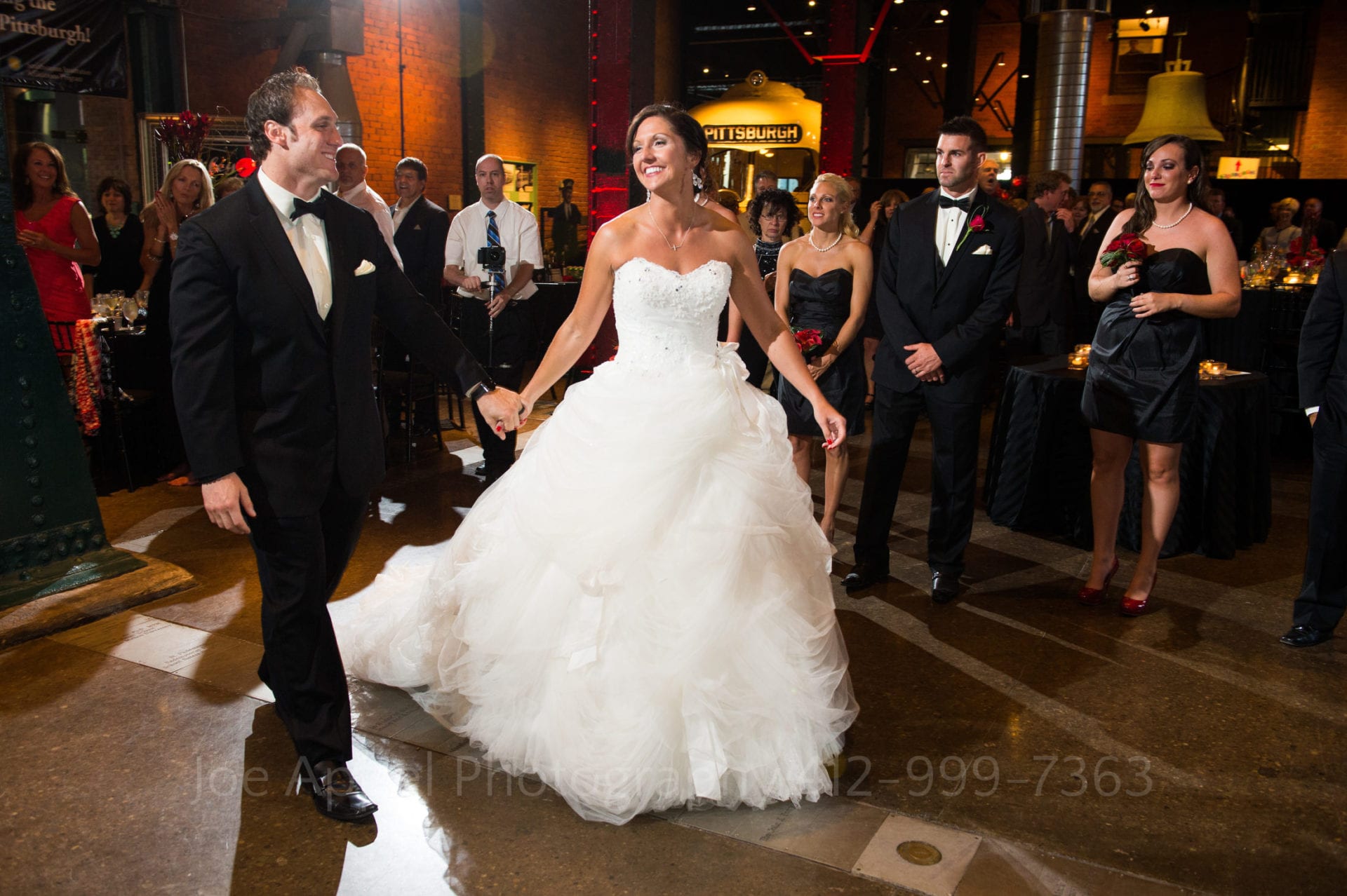 A bride and groom hold hands and walk on to the dance floor at the Heinz History Center.