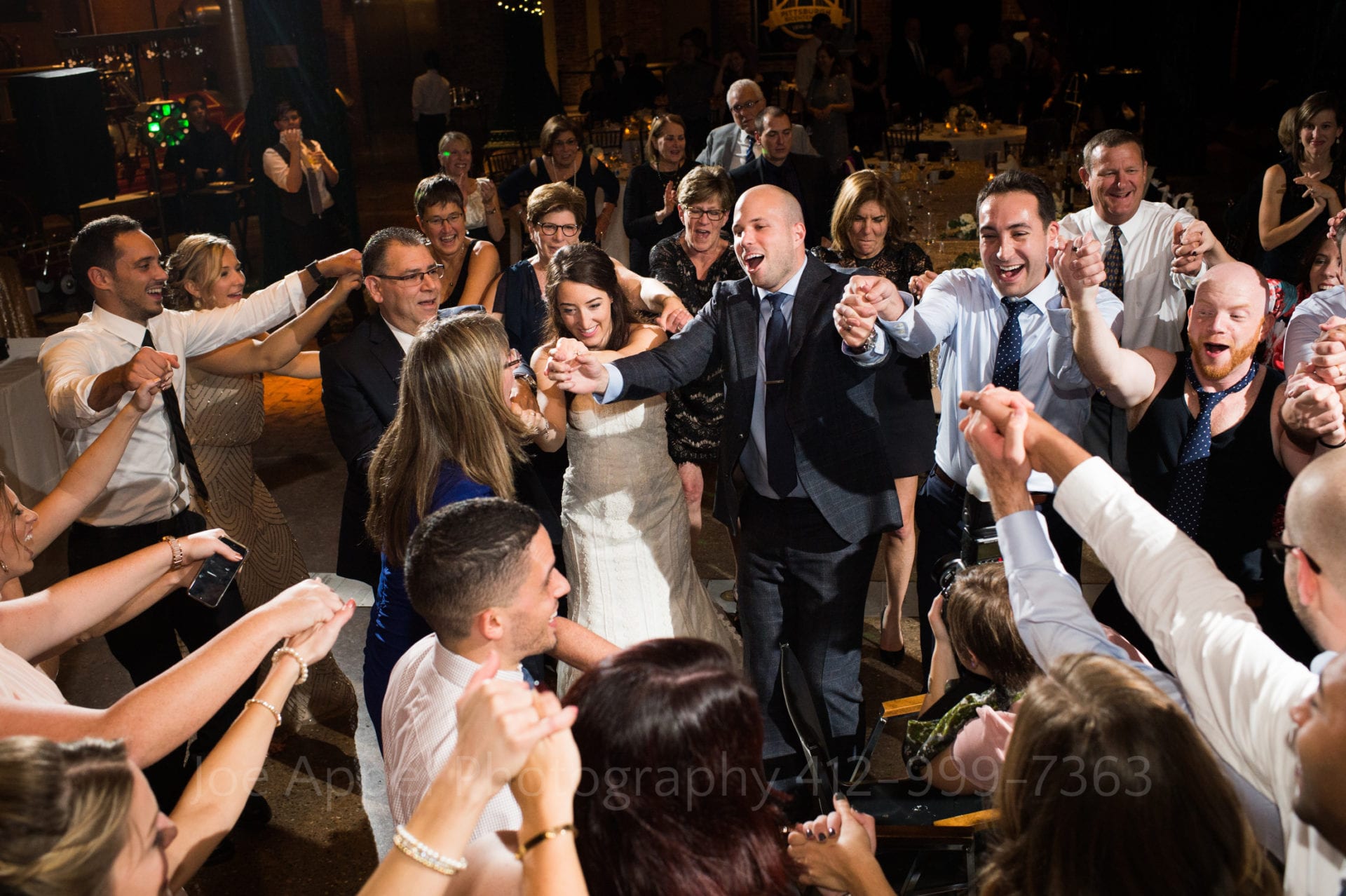 A bride and groom hold hands with their guests as they dance. Photo is seen from above.