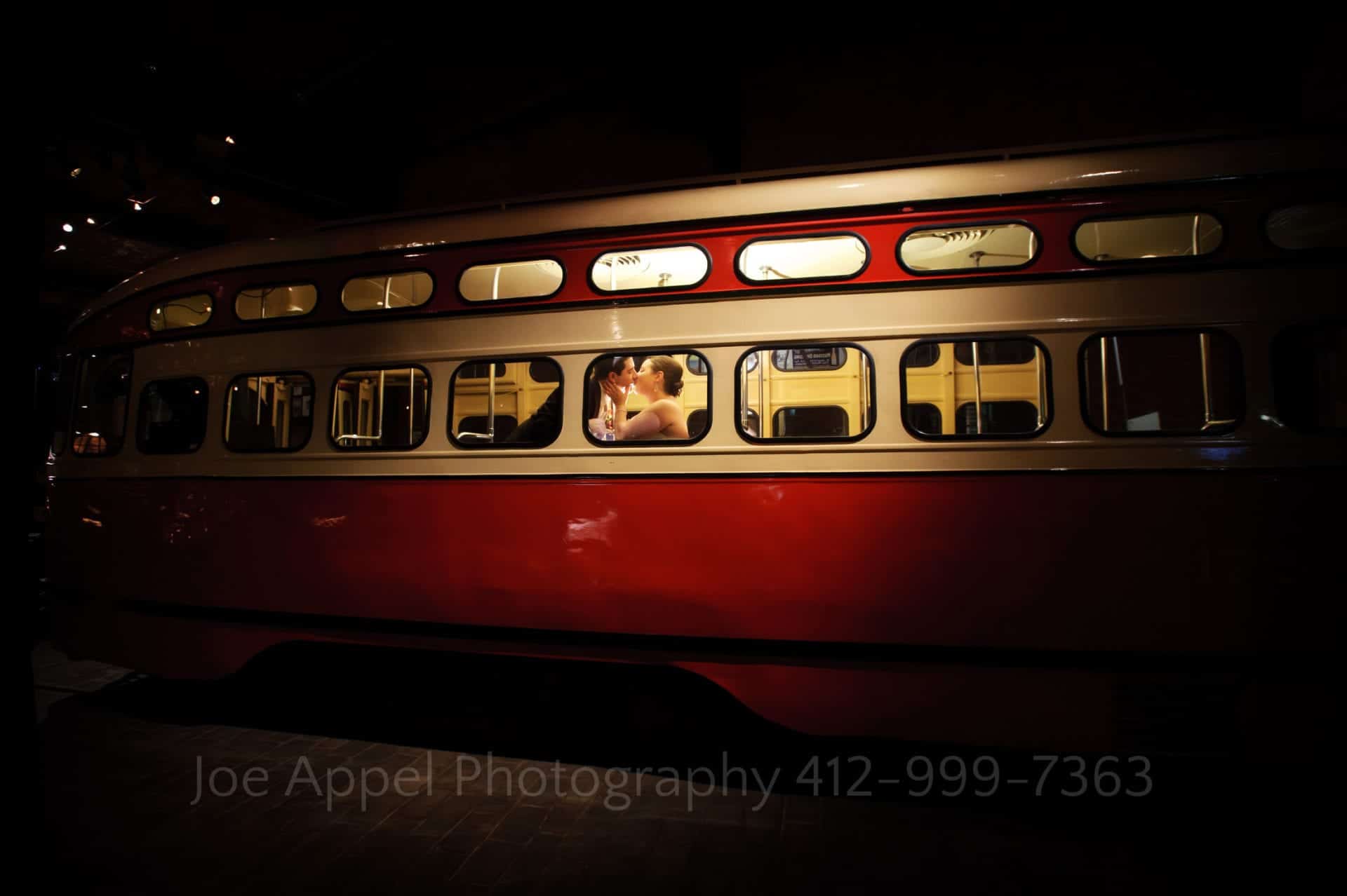 A couple kisses in the window of a red trolley car in the Great Hall at the Heinz History Center.