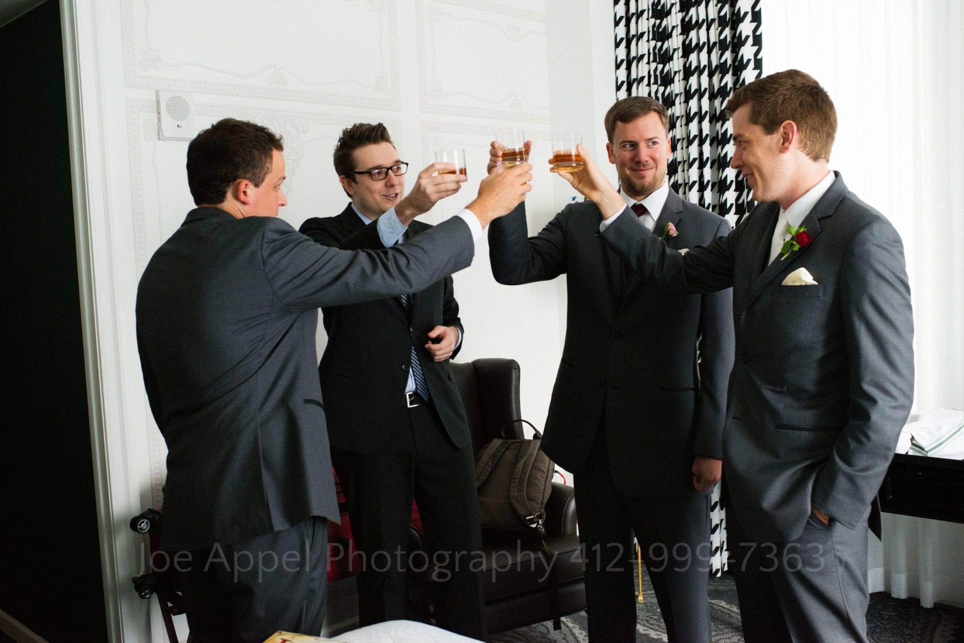 a group of groomsmen in tuxedos make a toast with scotch
