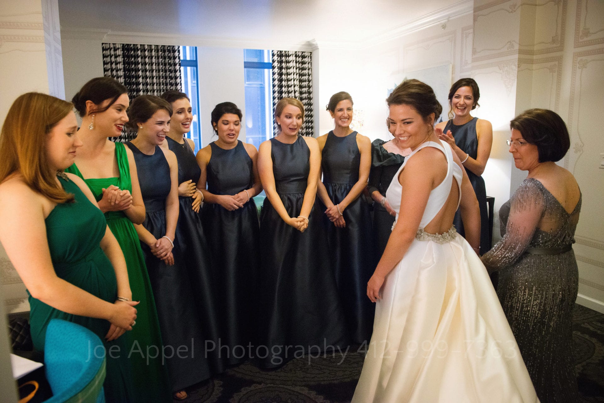 bridesmaids in blue and green dresses react to the bride's wedding day ensemble