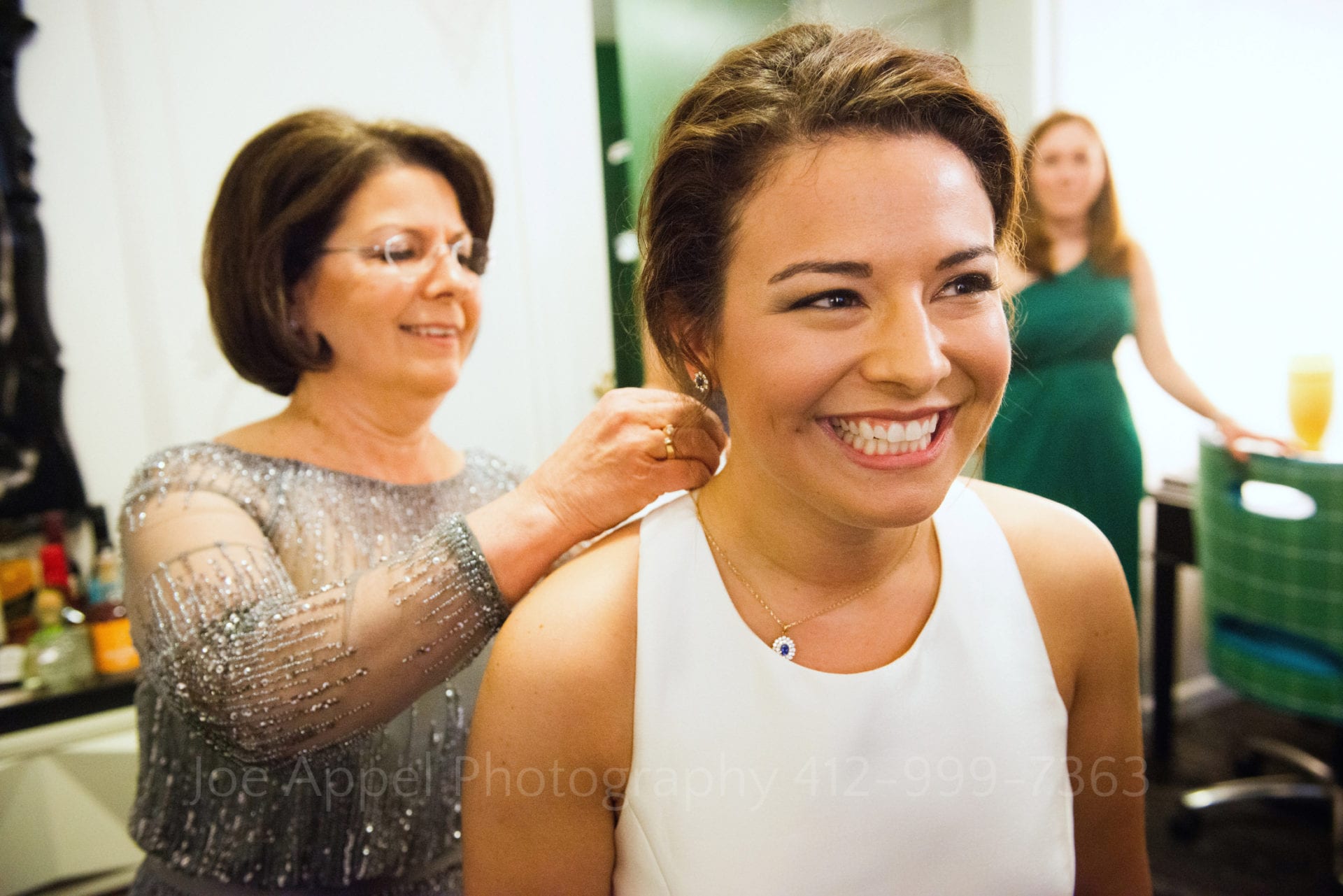 a bride smiles as her mother fastens a sapphire necklace on her