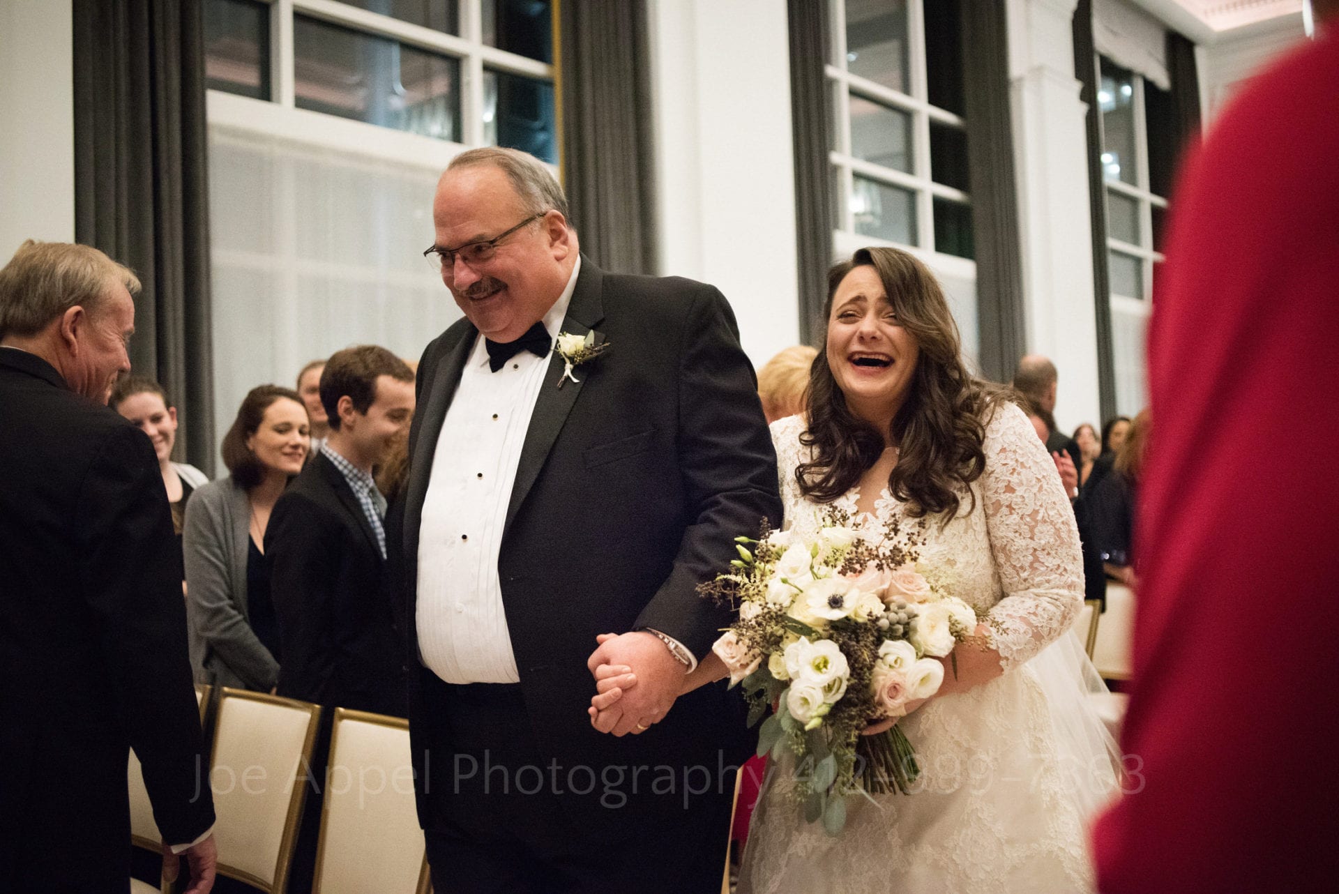 a bride smiles and carries a bouquet of pink and white poppies and roses as her father walks her down the aisle