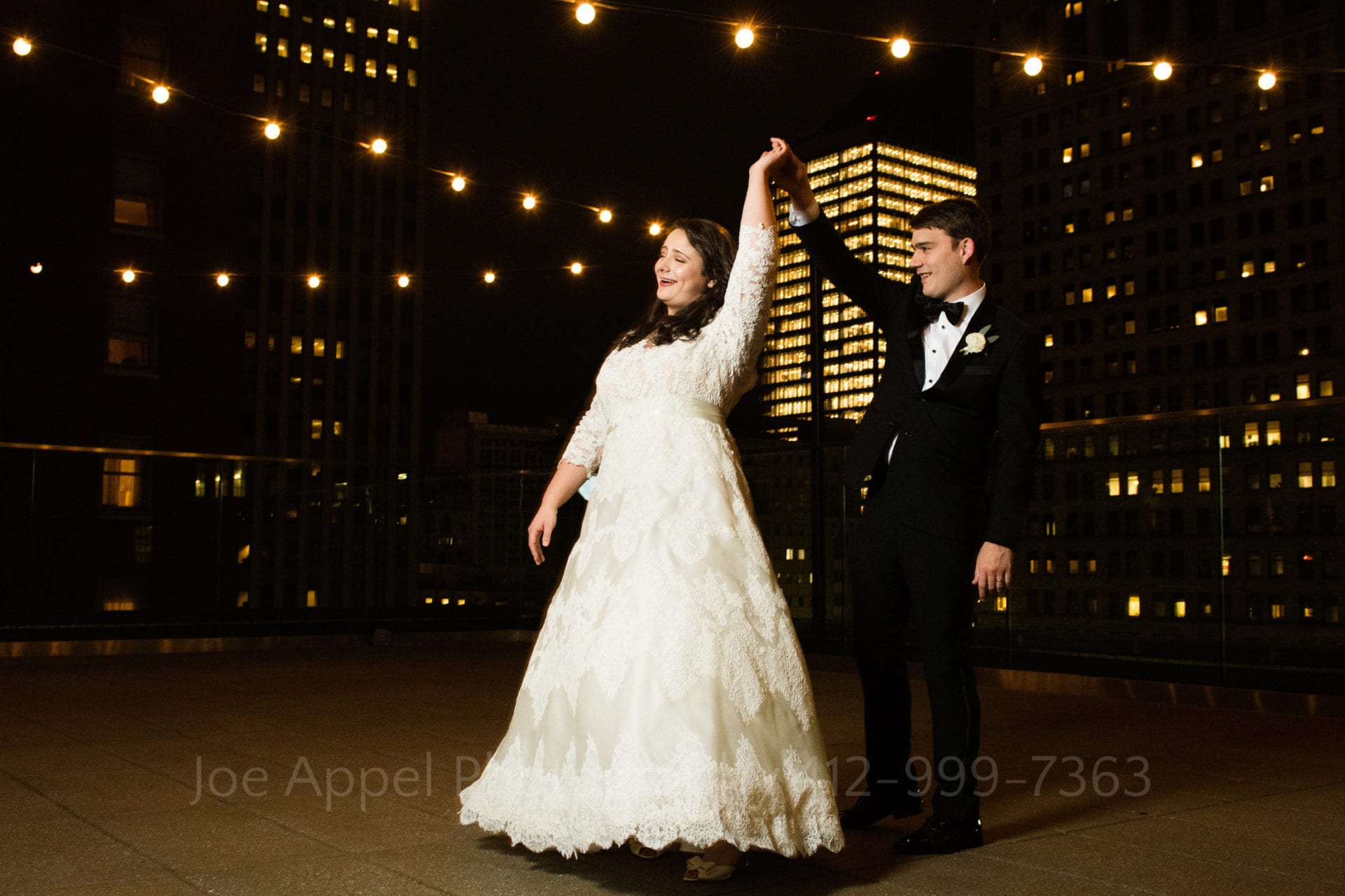 a bride and groom dance on a rooftop overlooking the city at nighttime