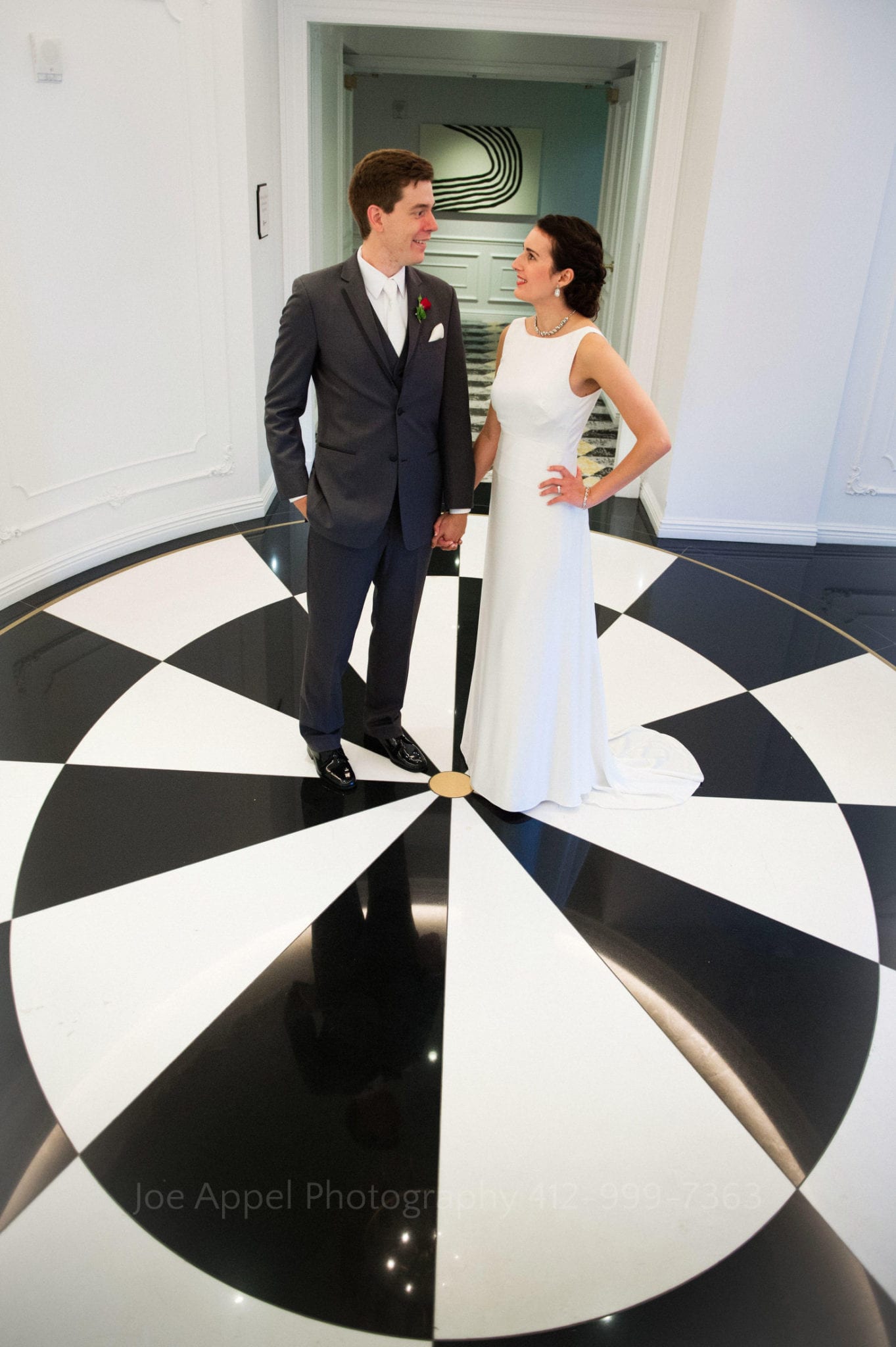 a bride and groom stand on top of a black and white checkerboard floor 