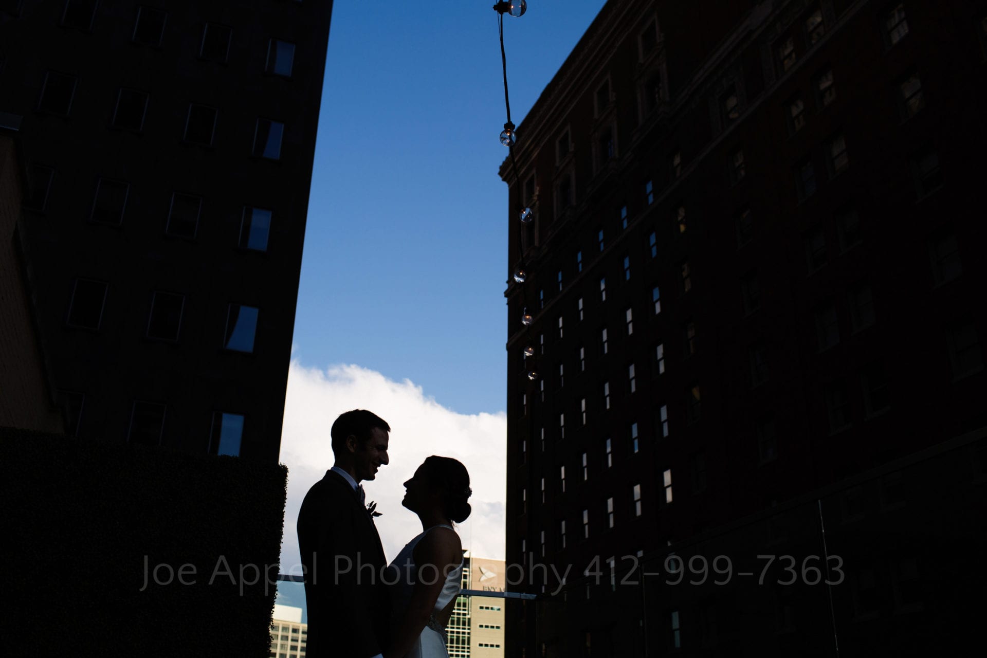 a bride and groom stand against a blue sky and city buildings