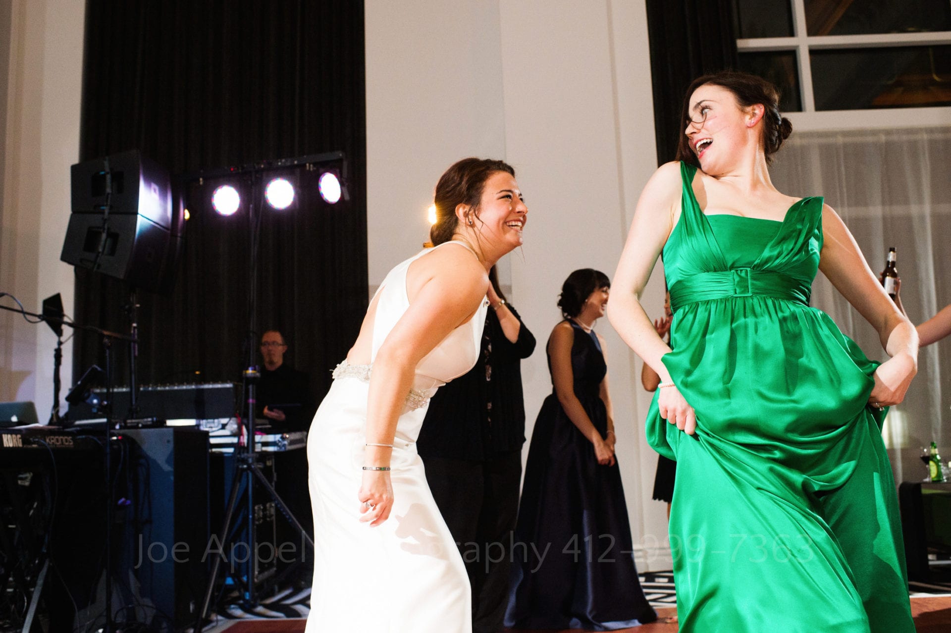 a bridesmaid in a green dress laughs and dances with the bride