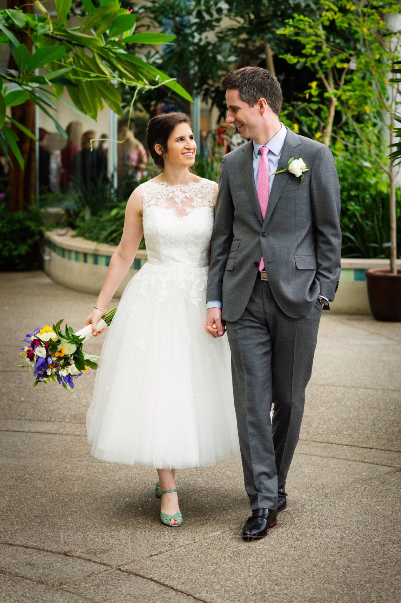 a bride with a colorful bouquet walks through a garden with her groom Phipps Conservatory Weddings