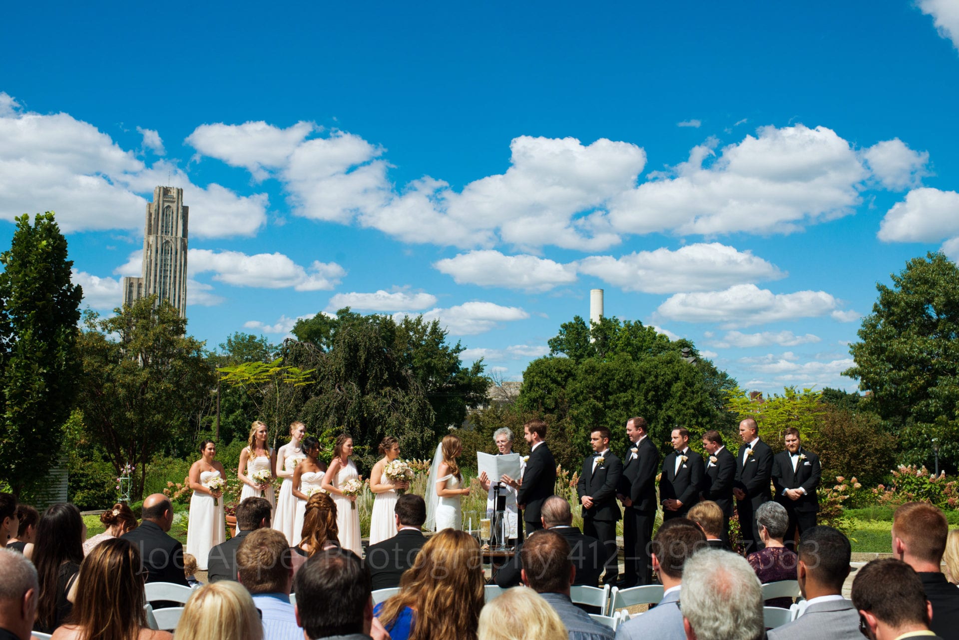 a wedding ceremony in front of a green forest and a blue sky with clouds Phipps Conservatory Weddings