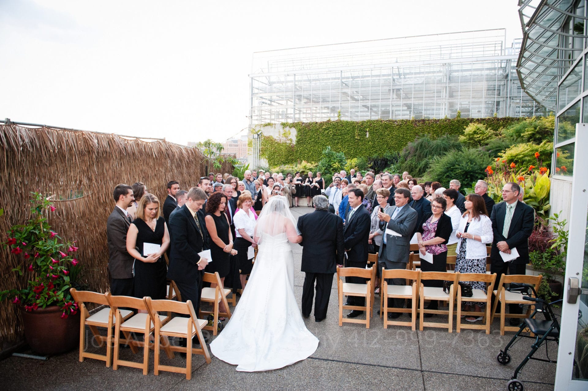 guests watch as a bride and her father walk down the aisle to a green garden Phipps Conservatory Weddings