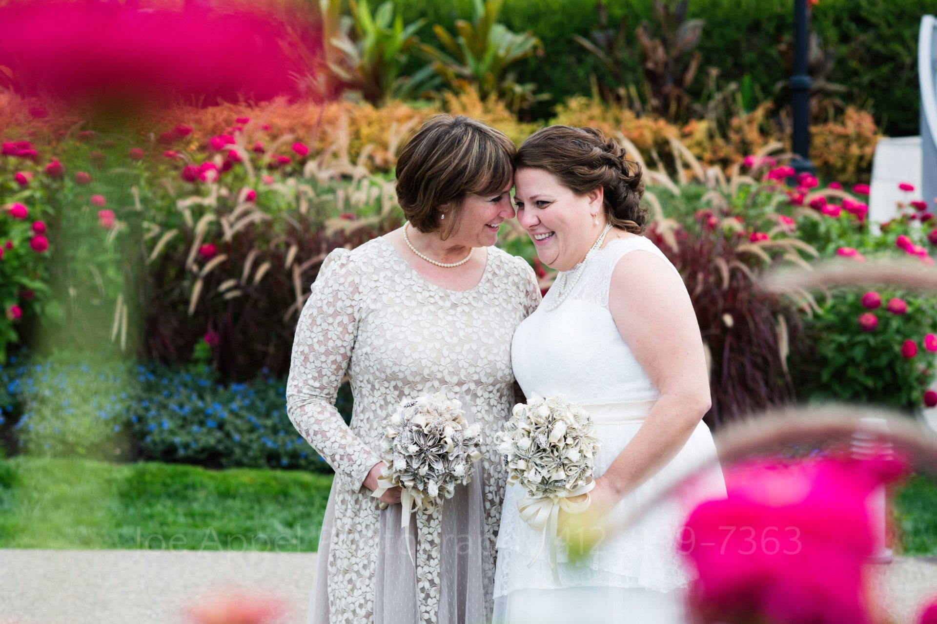 two brides smile in front of pink and blue flowers Phipps Conservatory Weddings