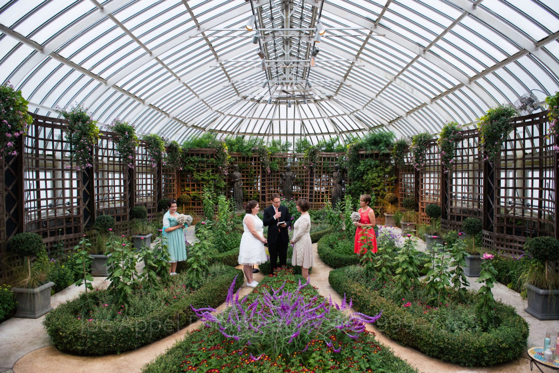 two brides say their vows in a green garden with purple flowers Phipps Conservatory Weddings