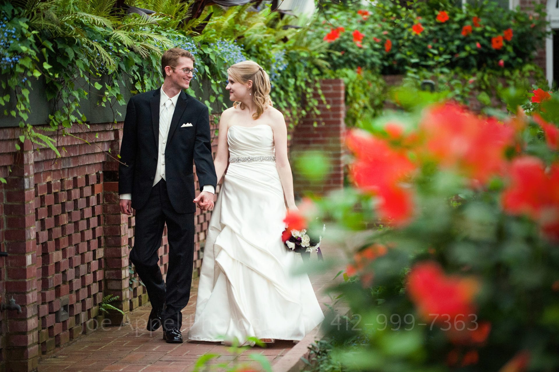 a bride and groom walk through a garden of leaves and red flowers Phipps Conservatory Weddings