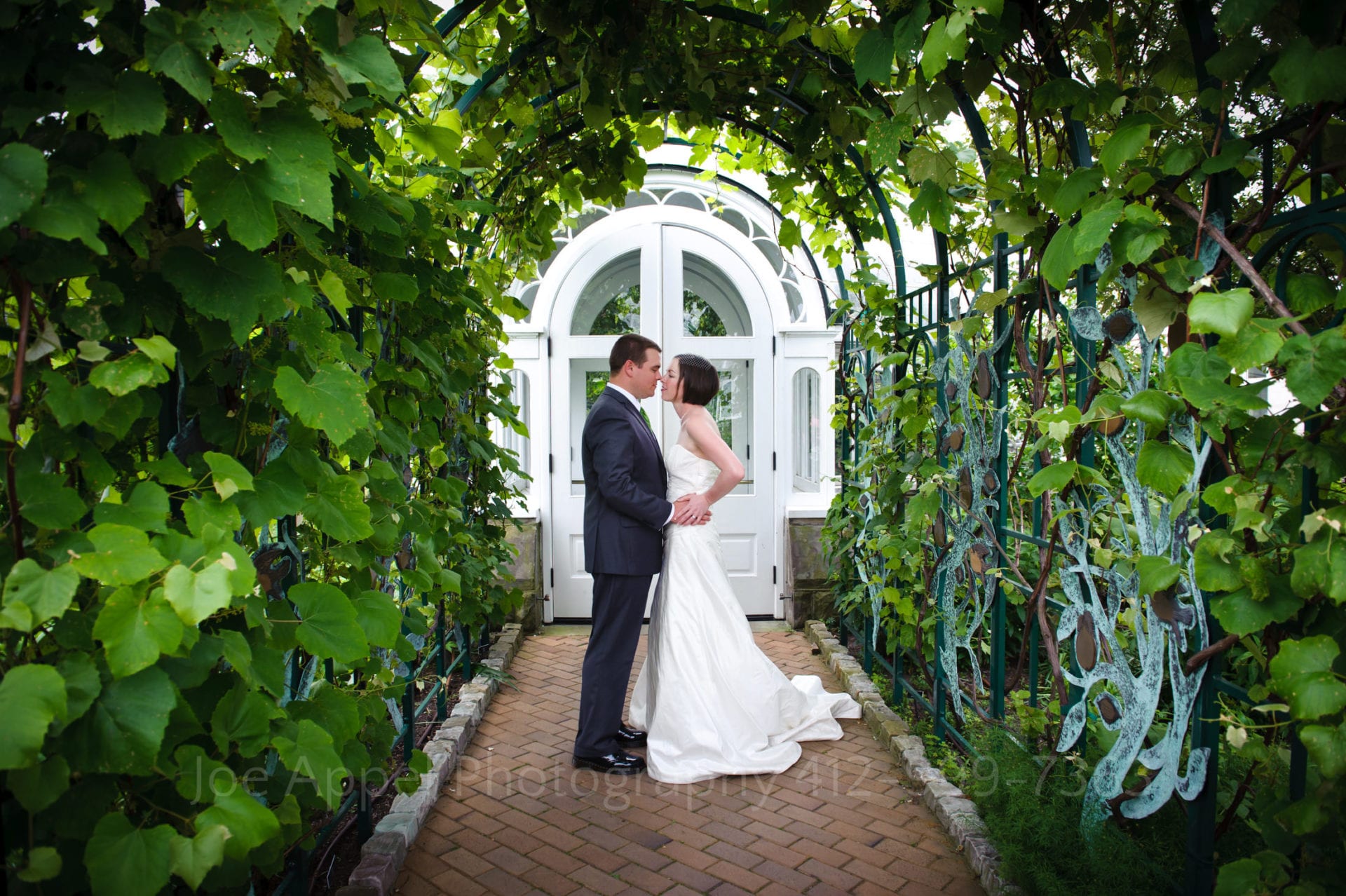 a bride and groom kiss under an arch of leaves Phipps Conservatory Weddings