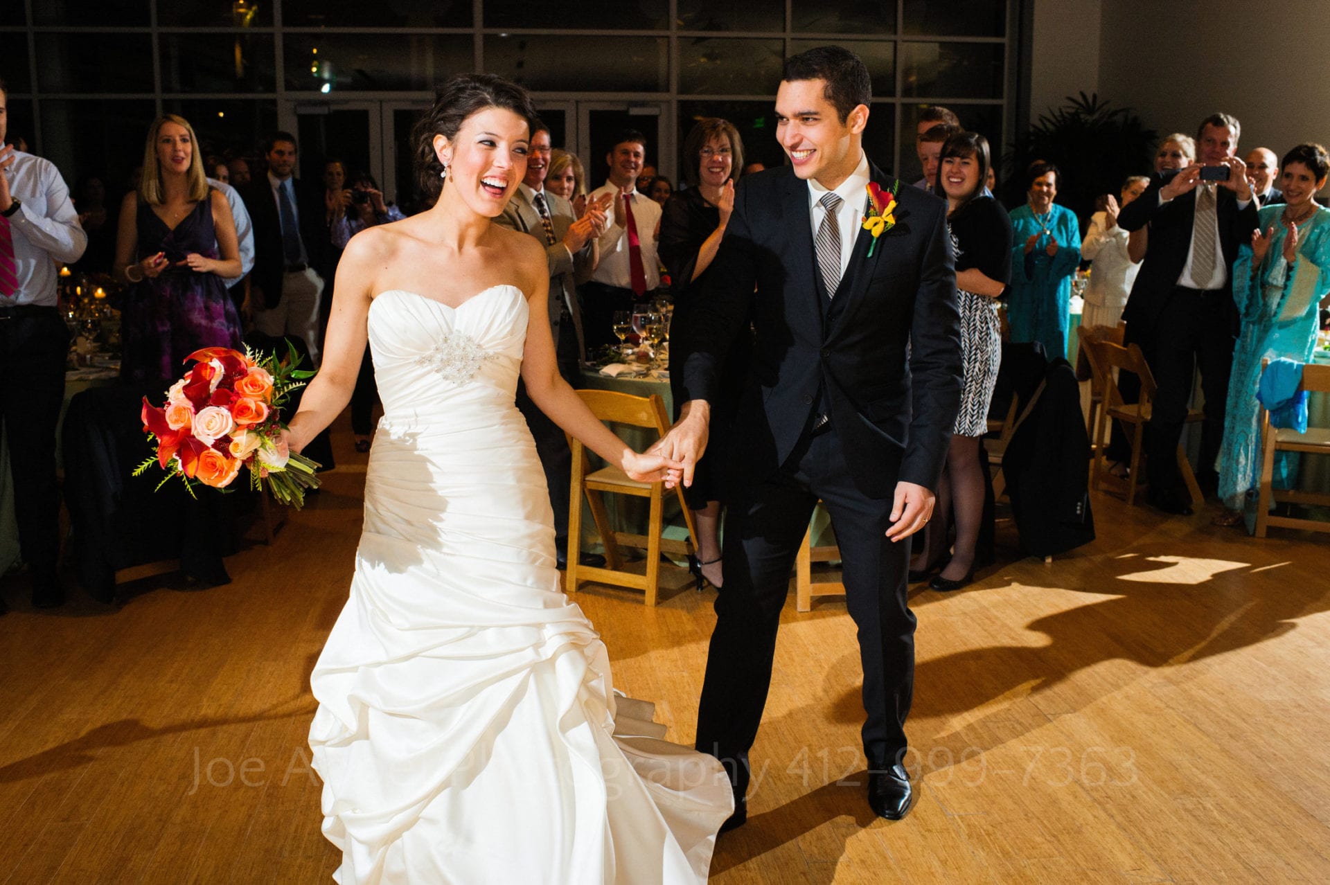 guests smile and watch a bride with an orange and pink bouquet dance with her groom Phipps Conservatory Weddings