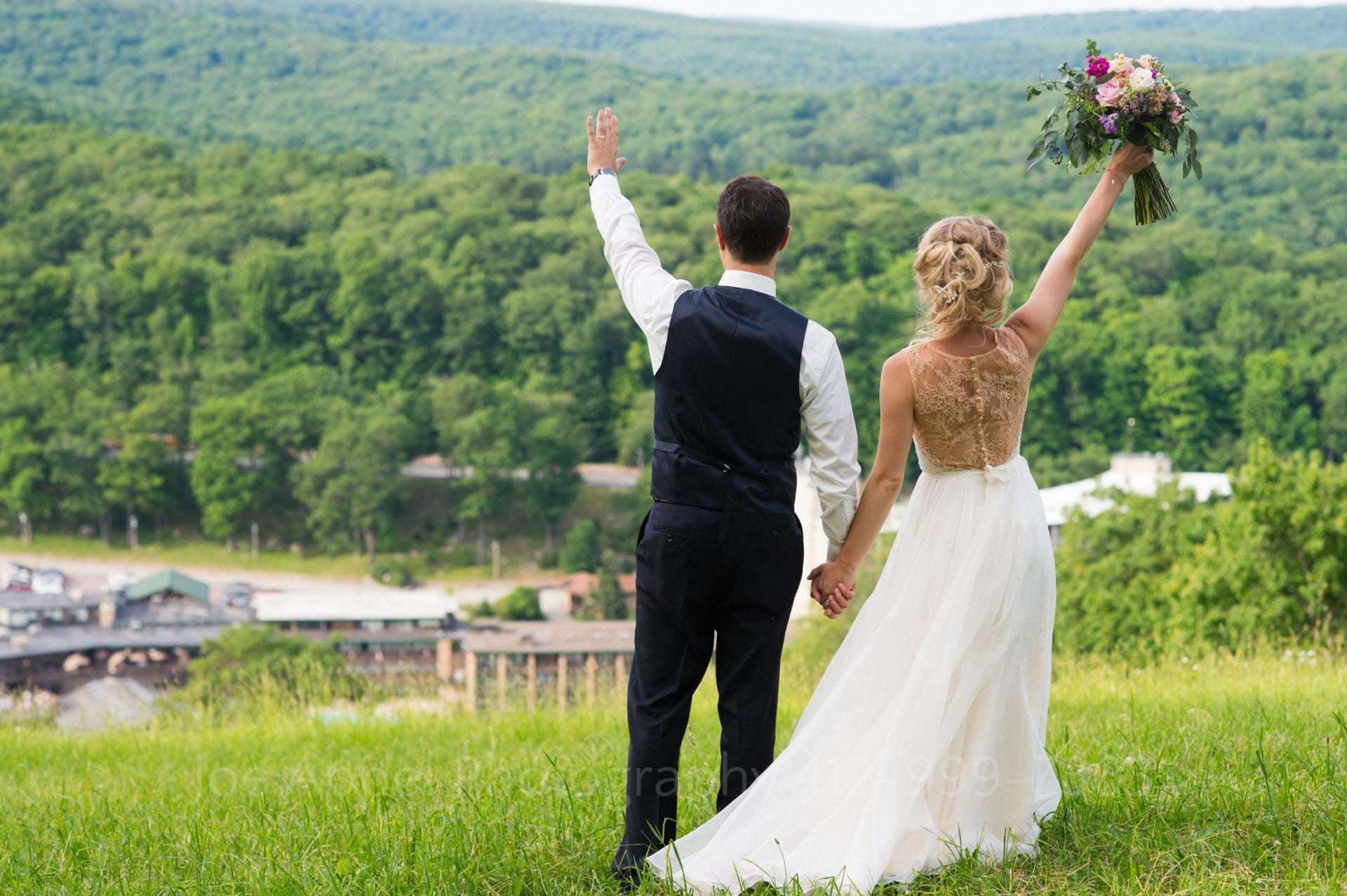 A bride and groom hold hands at the top of a mountain overlooking Seven Springs resort. They wave at the people far below them. Seven Springs Weddings