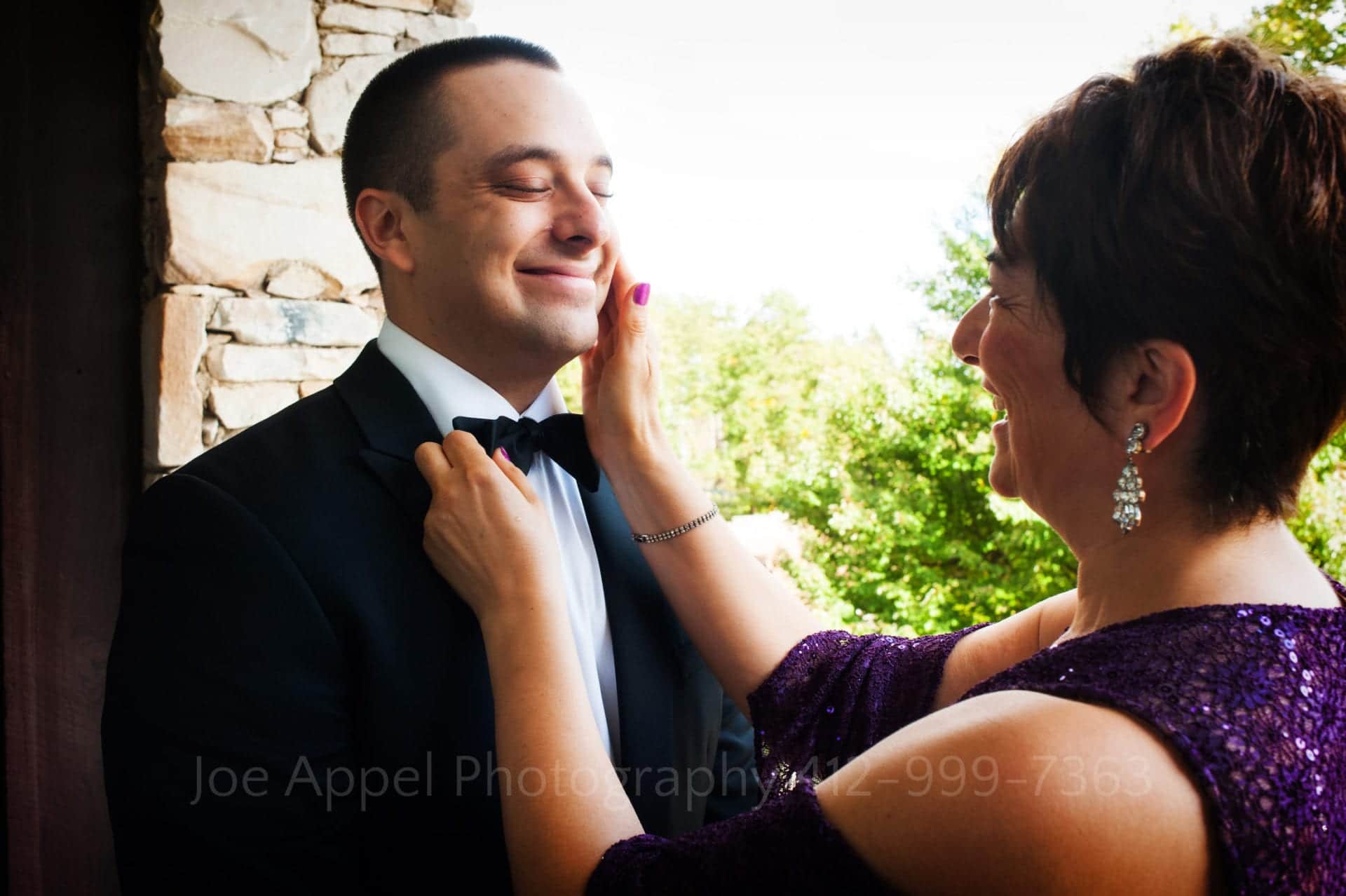a groom smiles as his mother touches his cheek Seven Springs Weddings