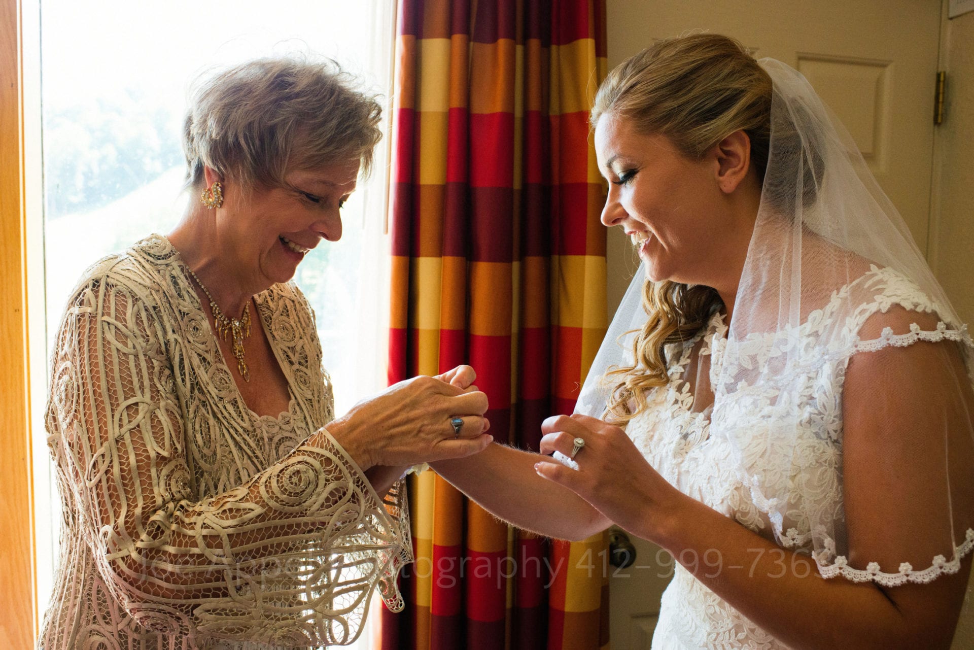 a brides mother fastens a bracelet on her daughter and they both smile Seven Springs Weddings