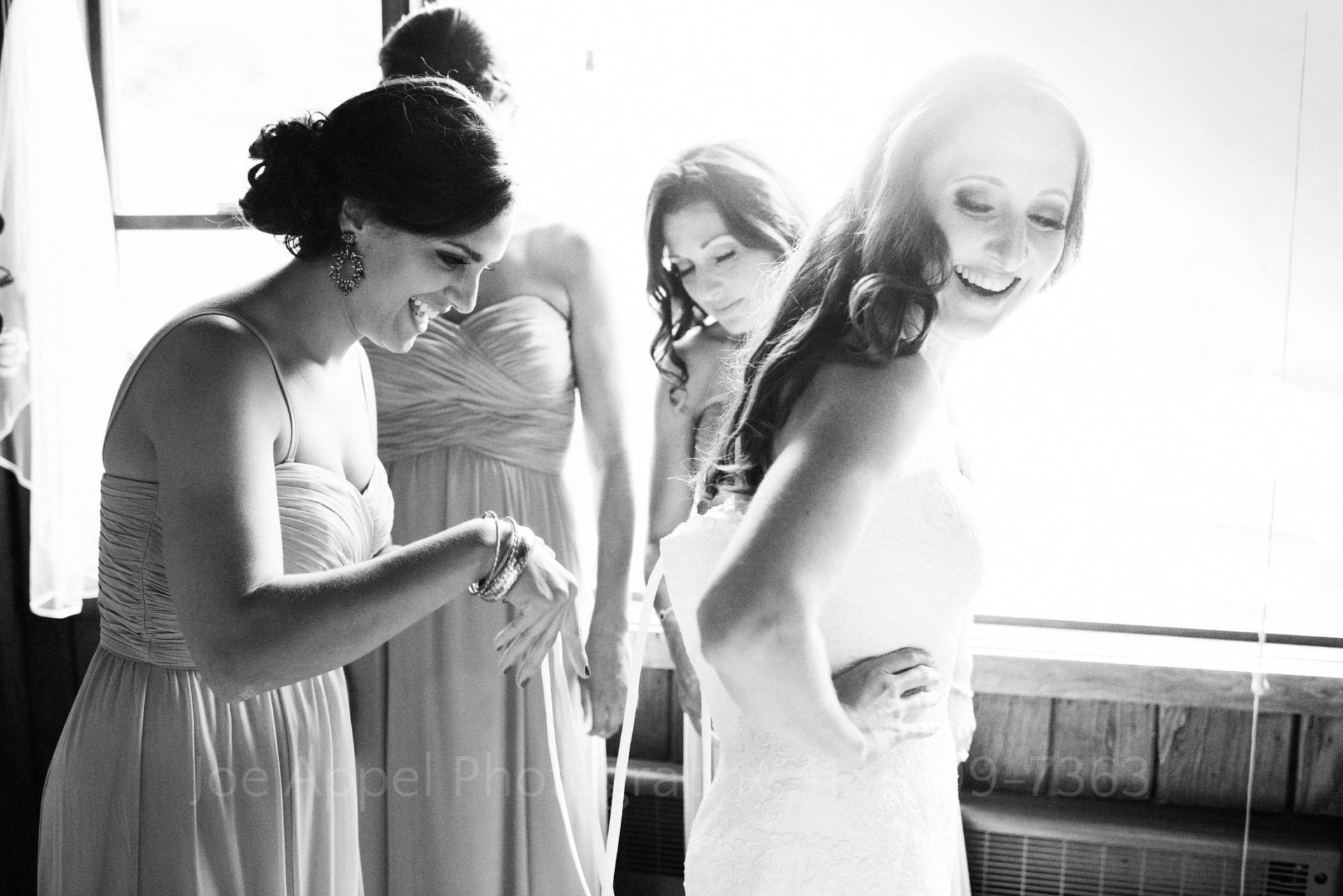 a bride laughs as her bridesmaids fasten her dress Seven Springs Weddings