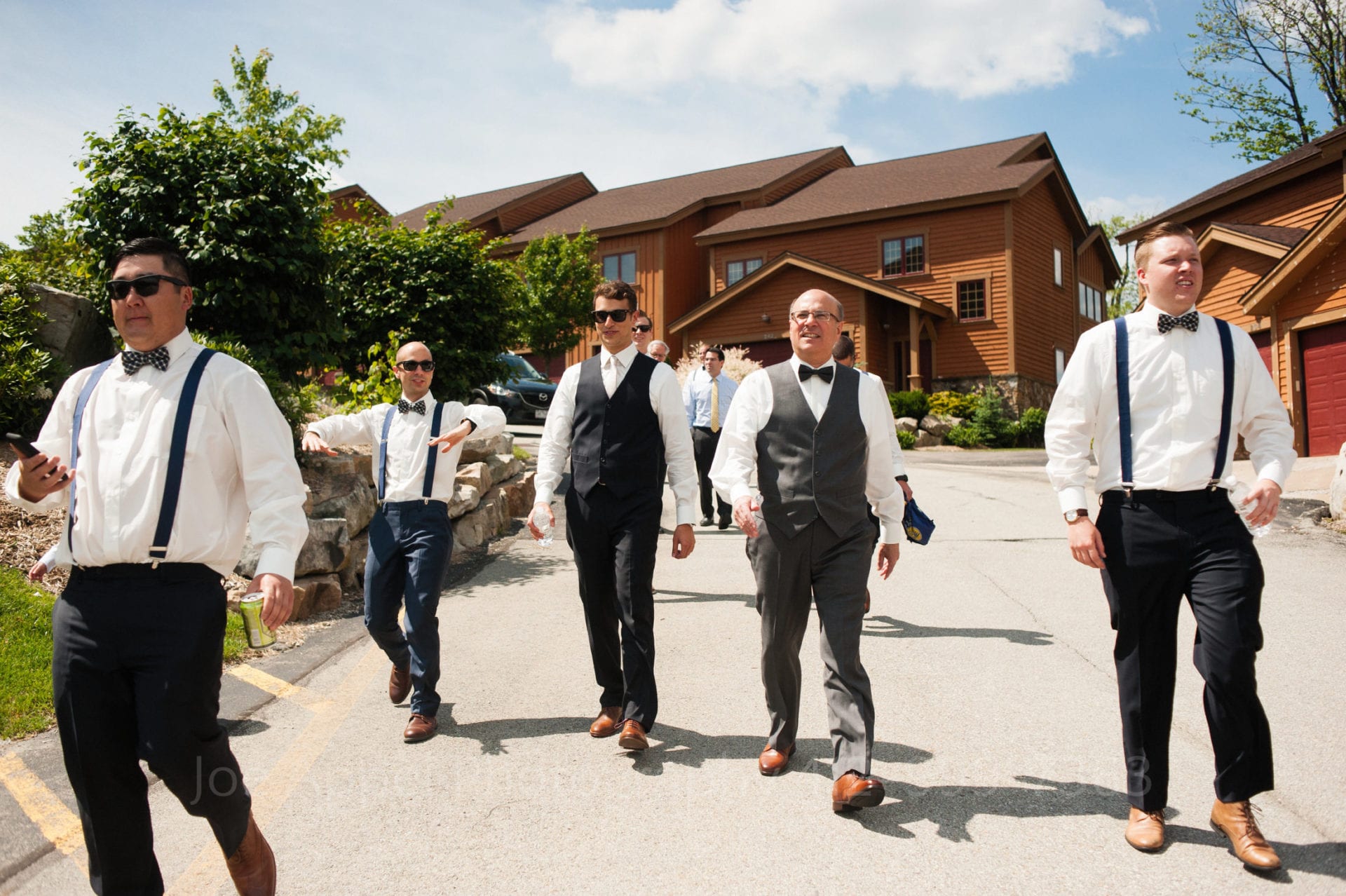 men wearing sunglasses and suspenders walk down a path with cabins behind them Seven Springs Weddings