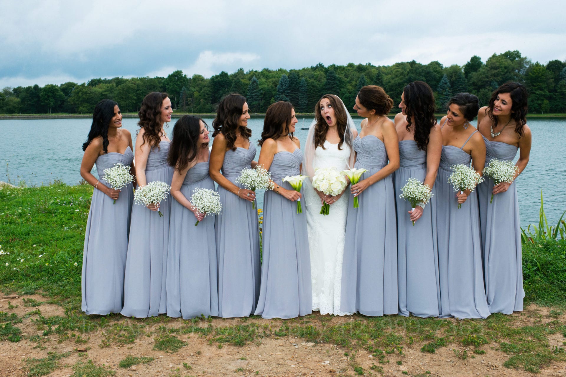 a bride stands in front of a lake with her bridesmaids in blue dresses Seven Springs Weddings