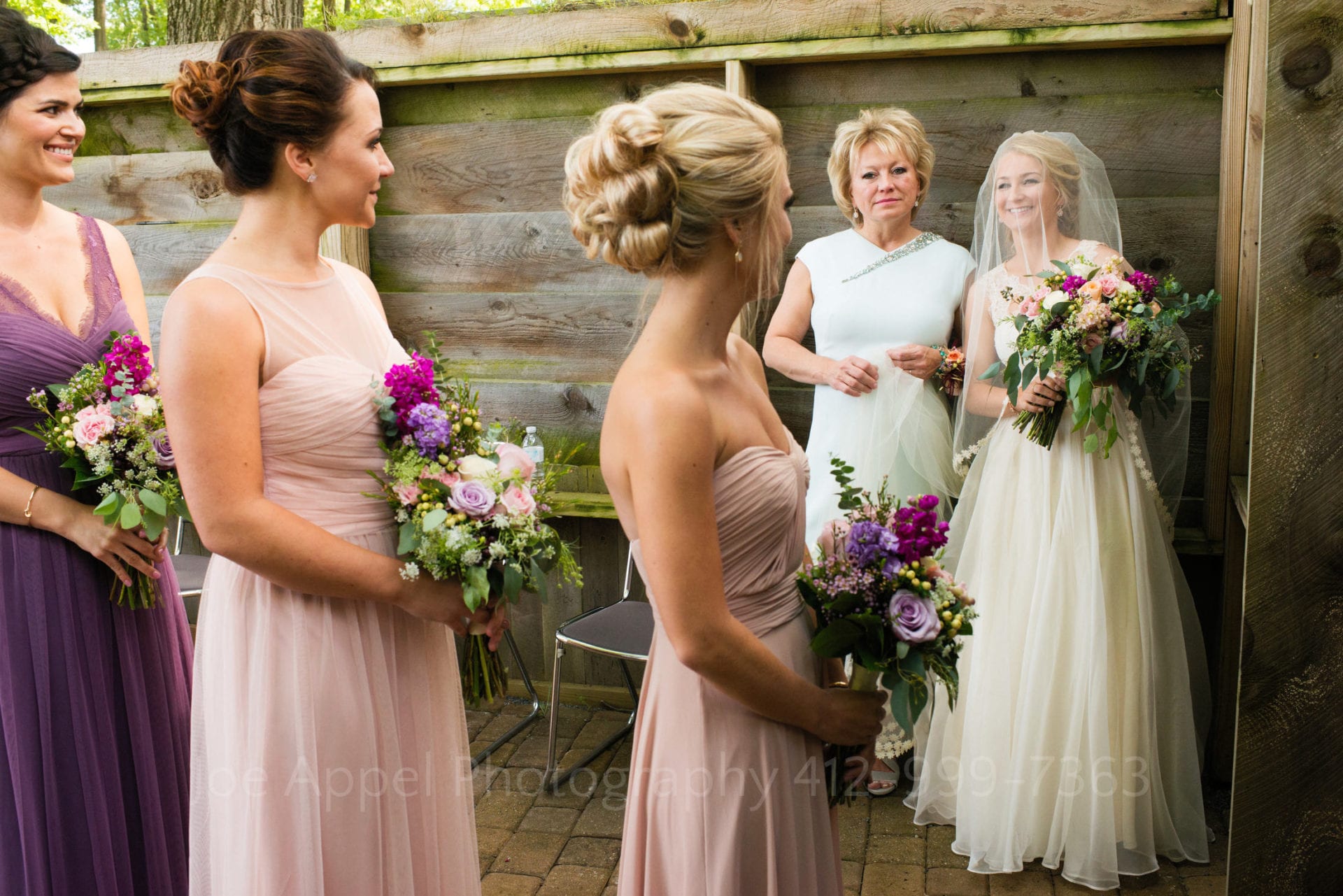 bridesmaids in pink and purple dresses with purple bouquets stand by a bride and her mother Seven Springs Weddings