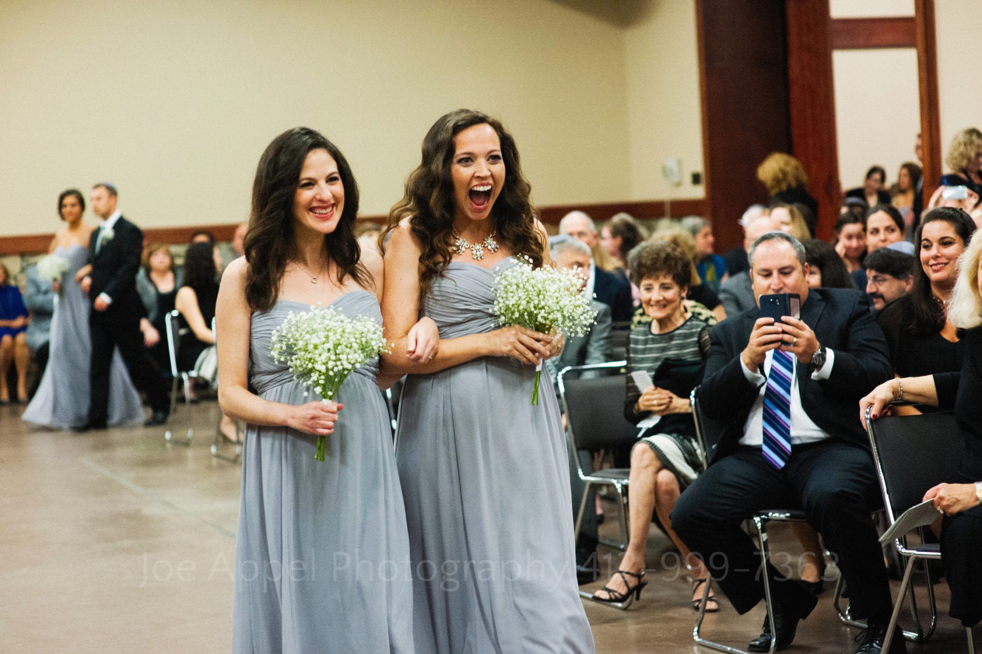 guests watch two smiling bridesmaids in gray dresses Seven Springs Weddings