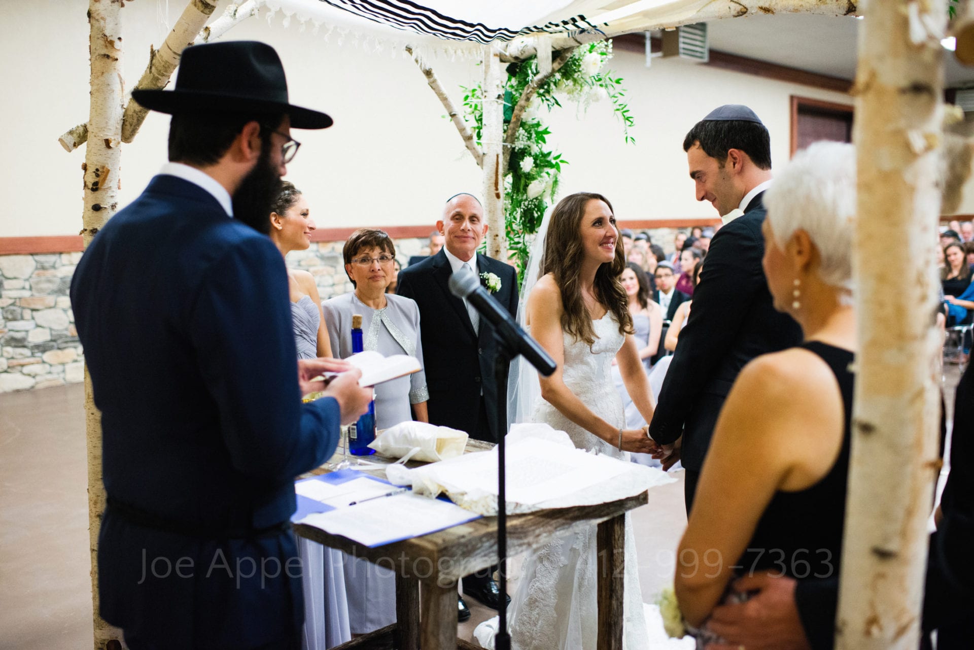 a bride and groom smile at each other underneath their chuppah Seven Springs Weddings