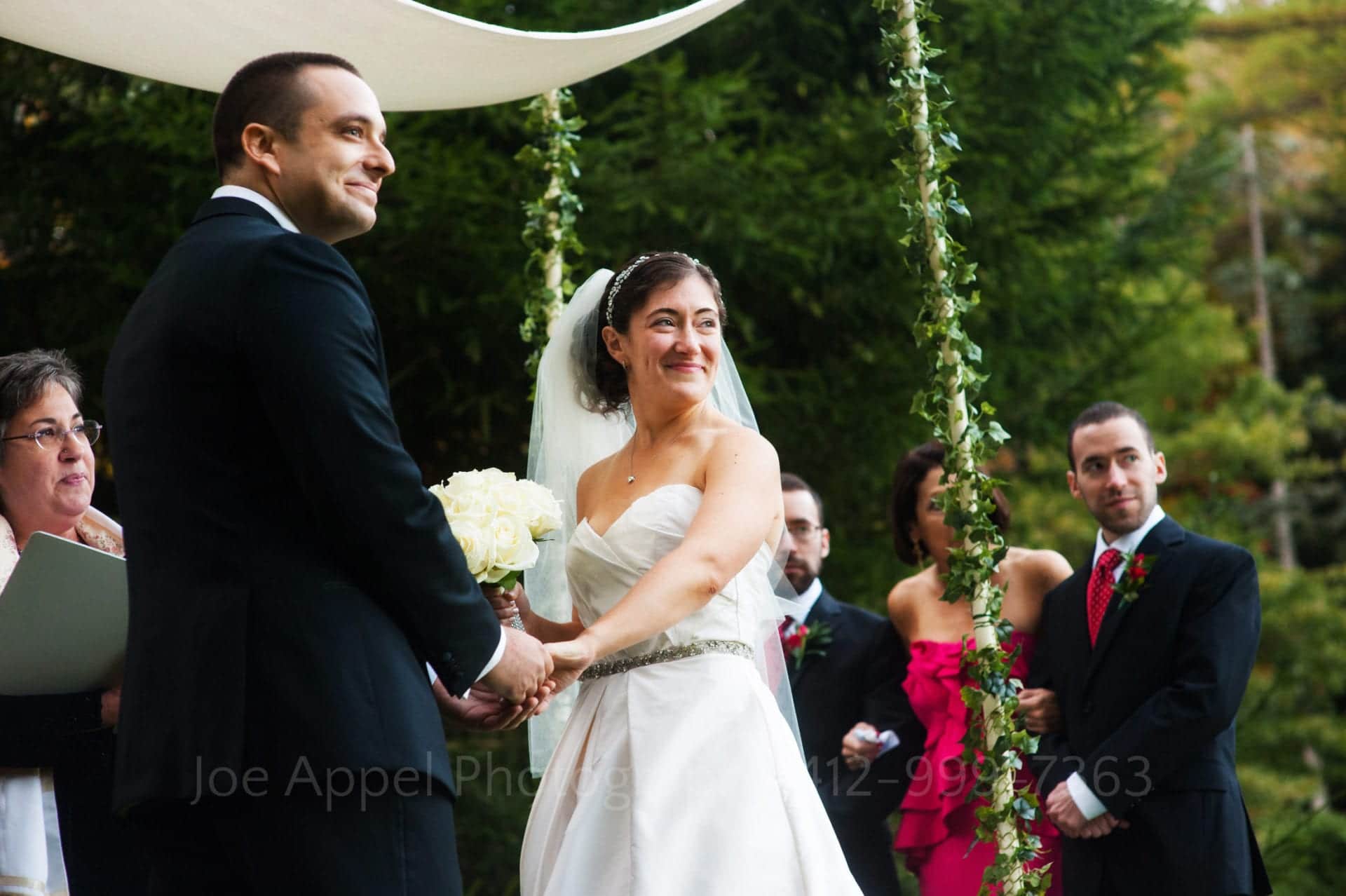 a bride and groom smile and hold hands under their chuppah Seven Springs Weddings